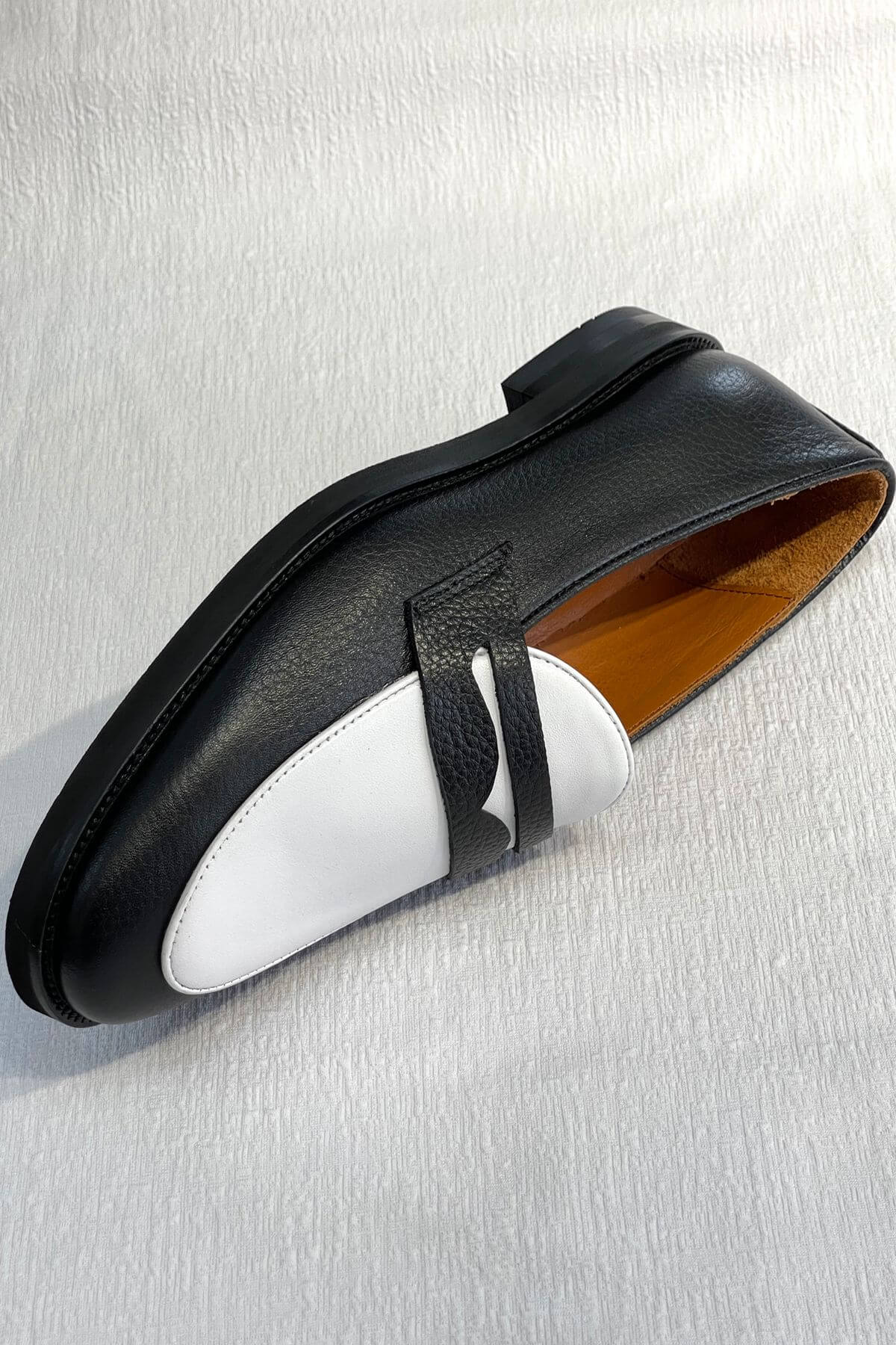Black loafer shoe with white sole on a light gray background