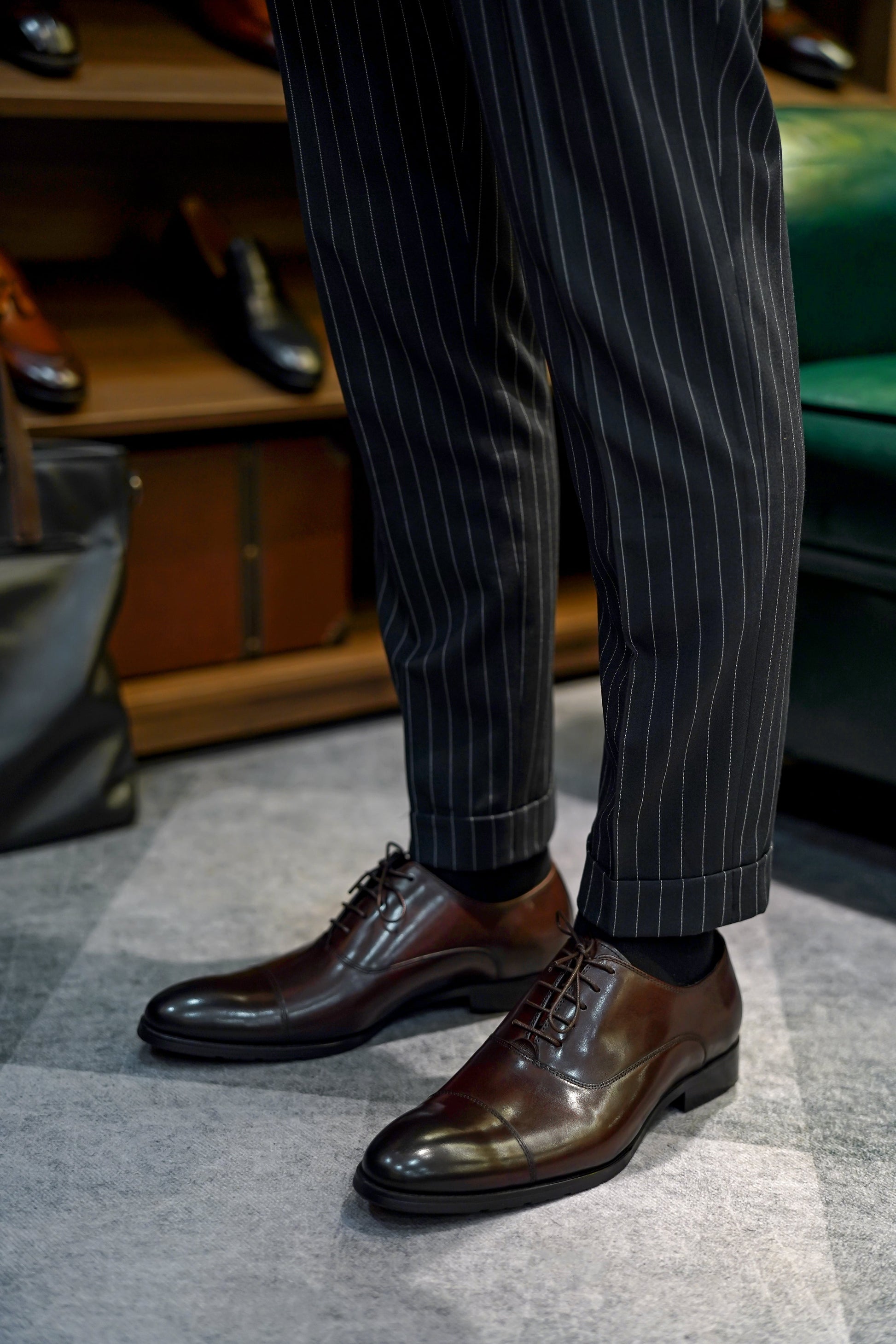 Close-up of men's espresso brown leather oxford shoes with a cap-toe design, worn with pinstriped trousers, showcasing premium craftsmanship and classic elegance for formal wear.