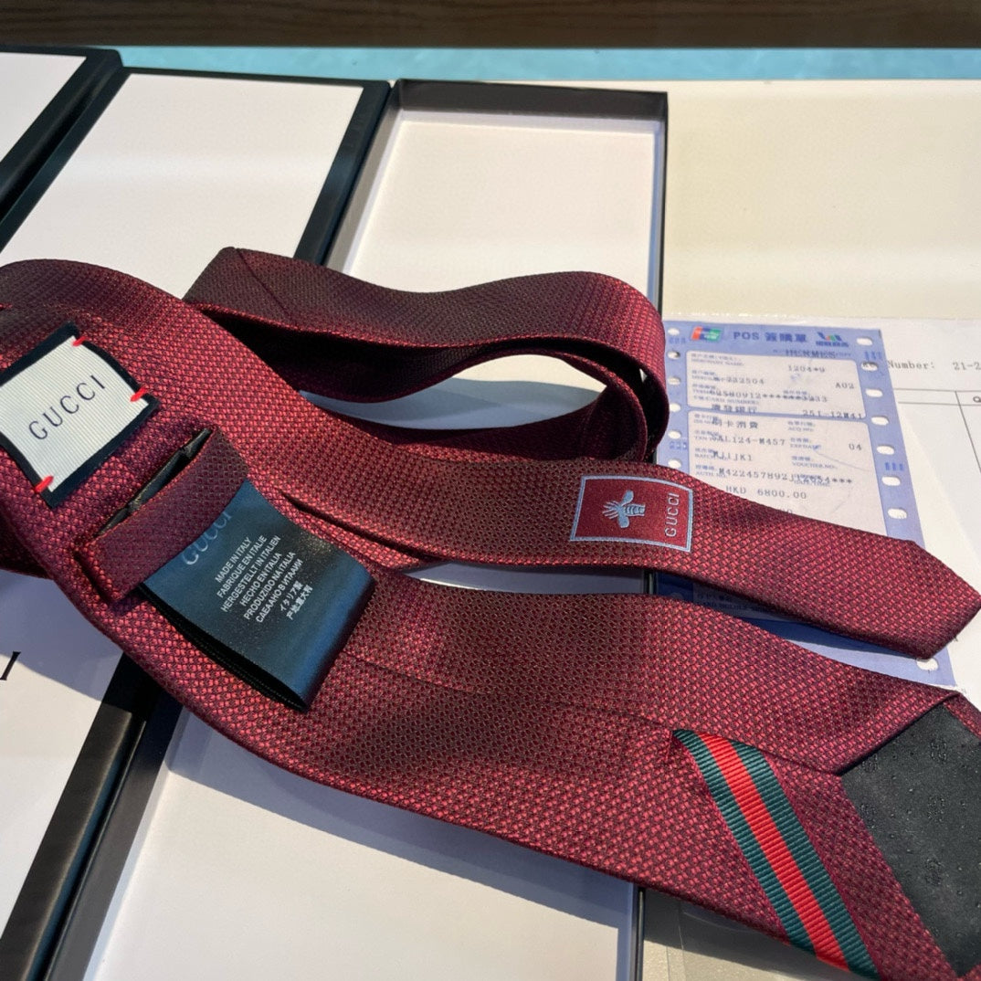 A burgundy silk tie with green and red stripes and a Gucci emblem, displayed on a table with a bill and a menu.