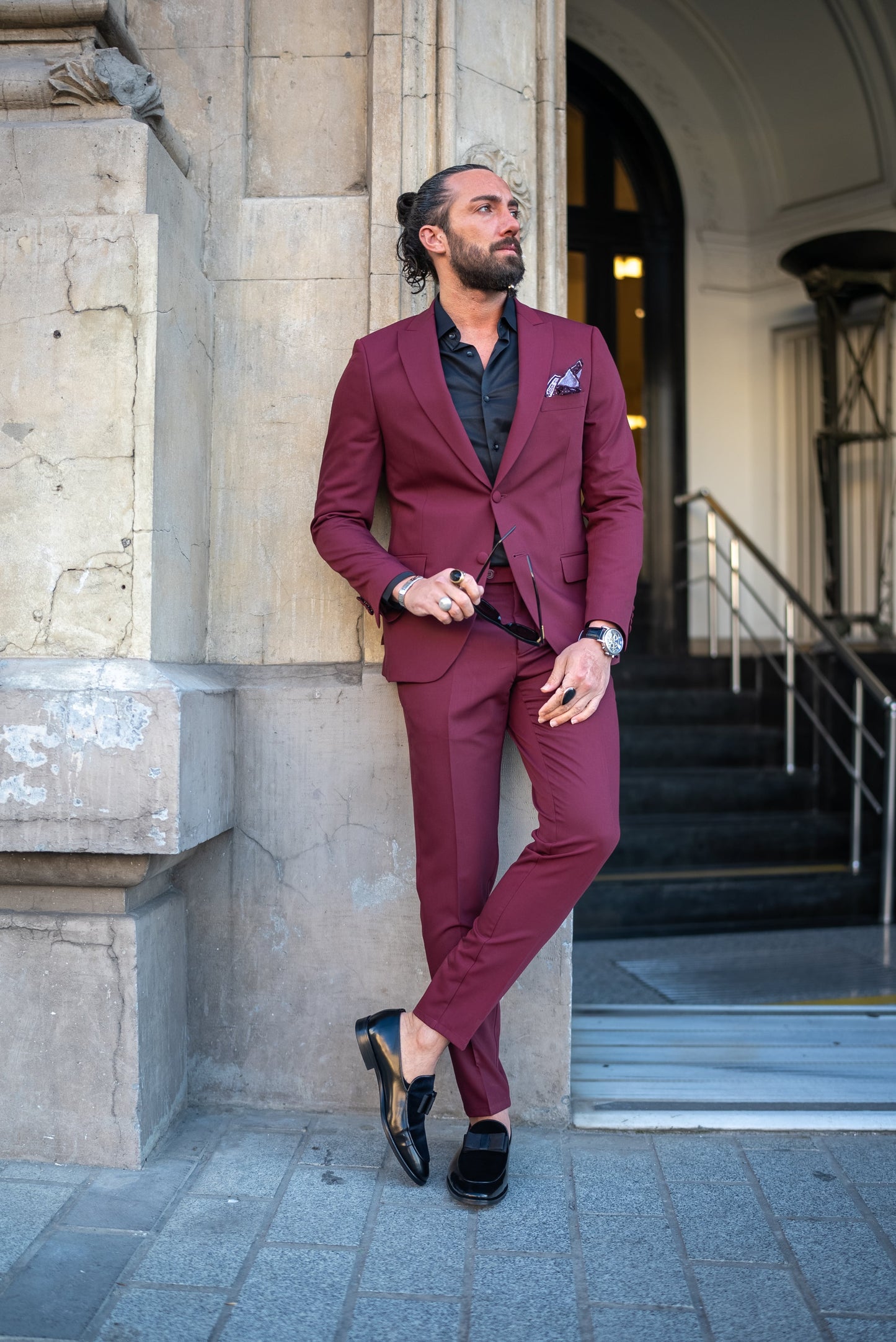 Man wearing a burgundy Italian cut tuxedo suit, paired with a black shirt, perfect for men's fall fashion and formal events.
