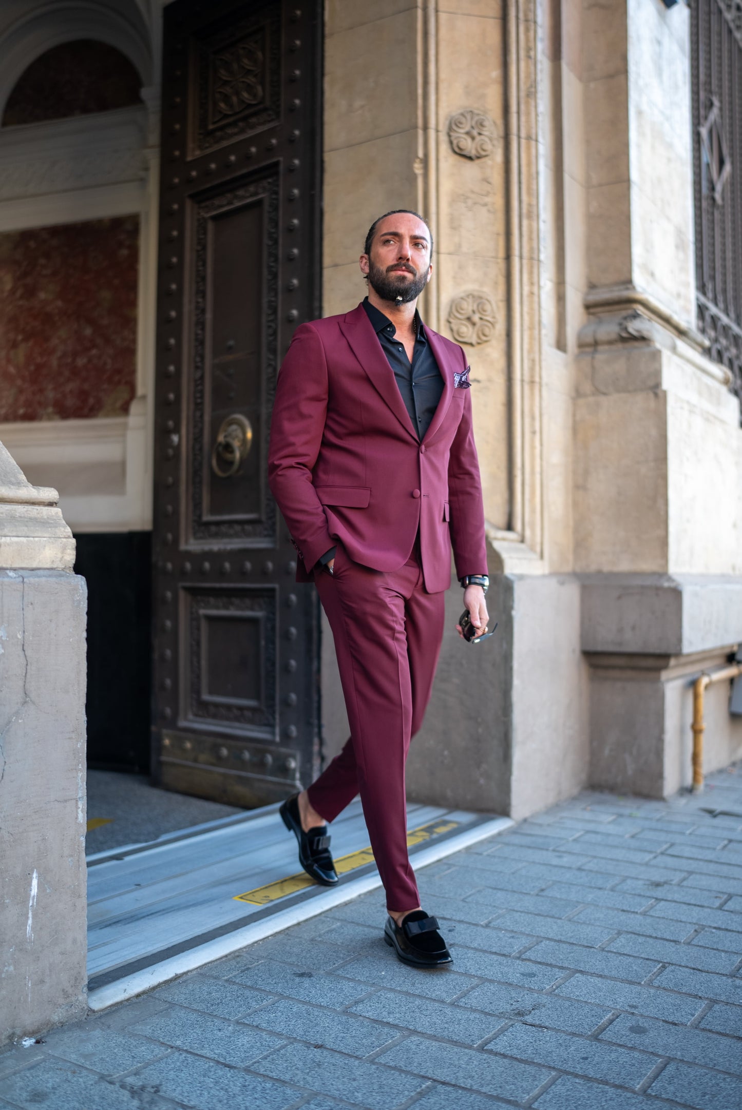 Man wearing a burgundy Italian cut tuxedo suit, paired with a black shirt, perfect for men's fall fashion and formal events.