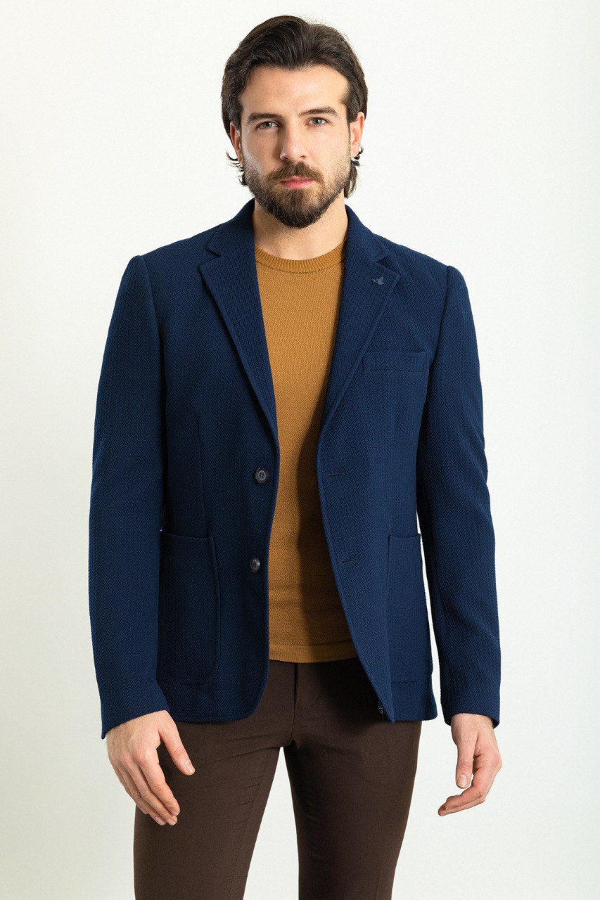 Man wearing a navy blue blazer paired with a mustard sweater and brown trousers.