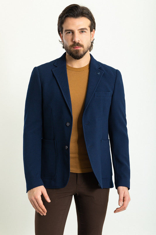 Man wearing a navy blue blazer paired with a mustard sweater and brown trousers.