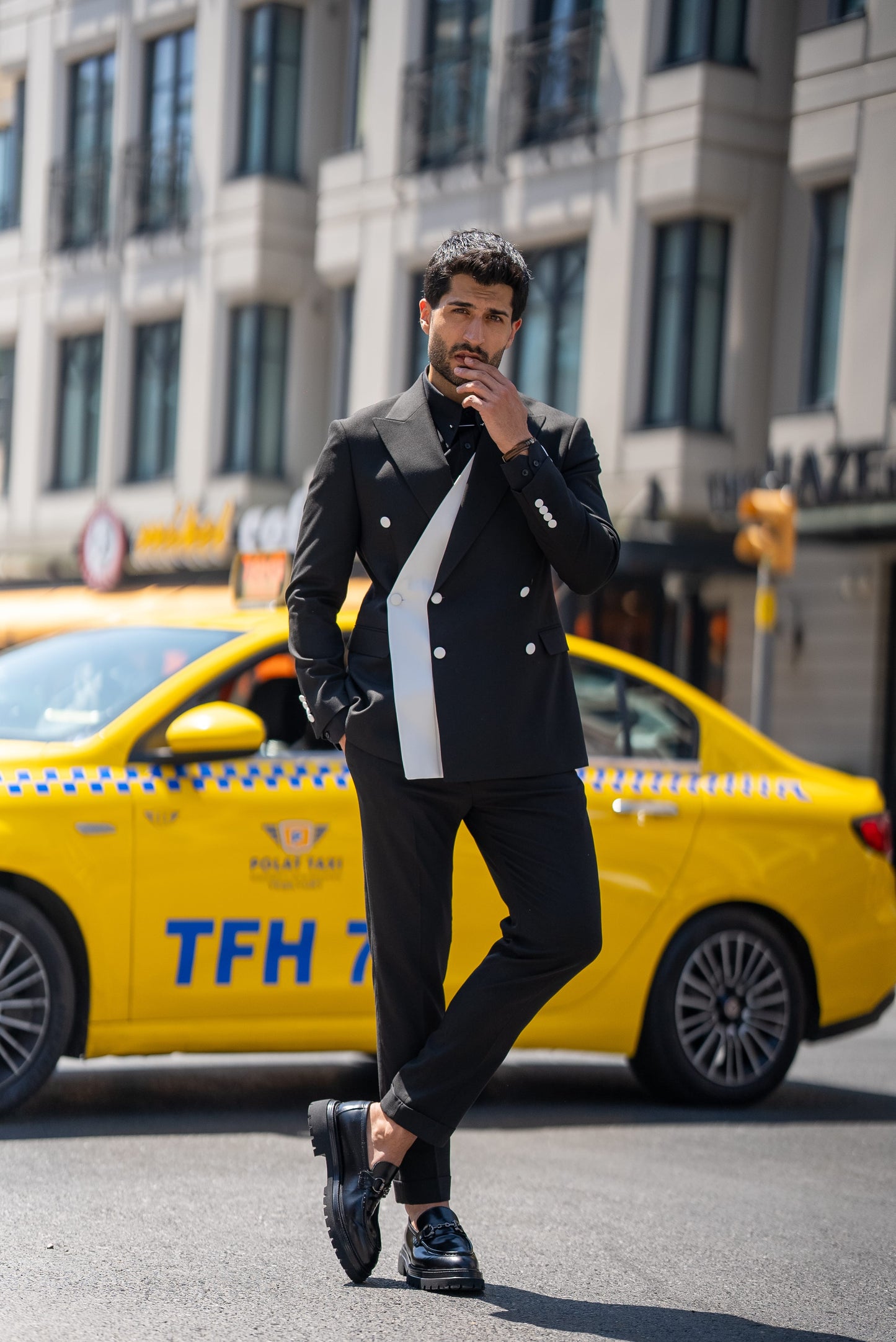 Man in a stylish outfit standing on a street with a yellow taxi in the background
