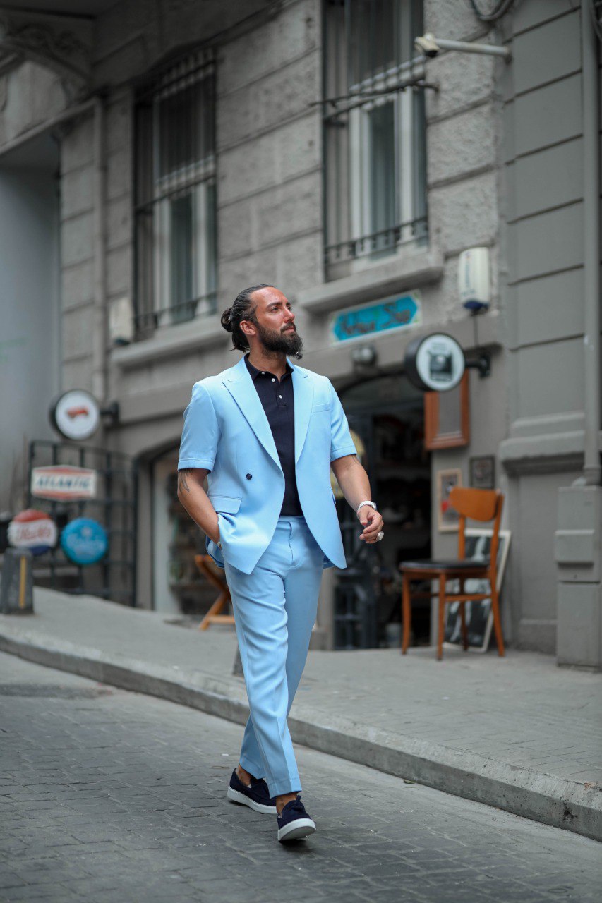Men in light blue summer suit leaning casually by doorway, wedding and party-ready attire.
