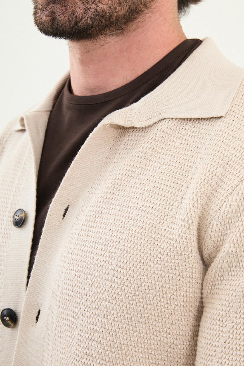 Close-up of a person wearing a beige textured coat with a brown shirt underneath.
