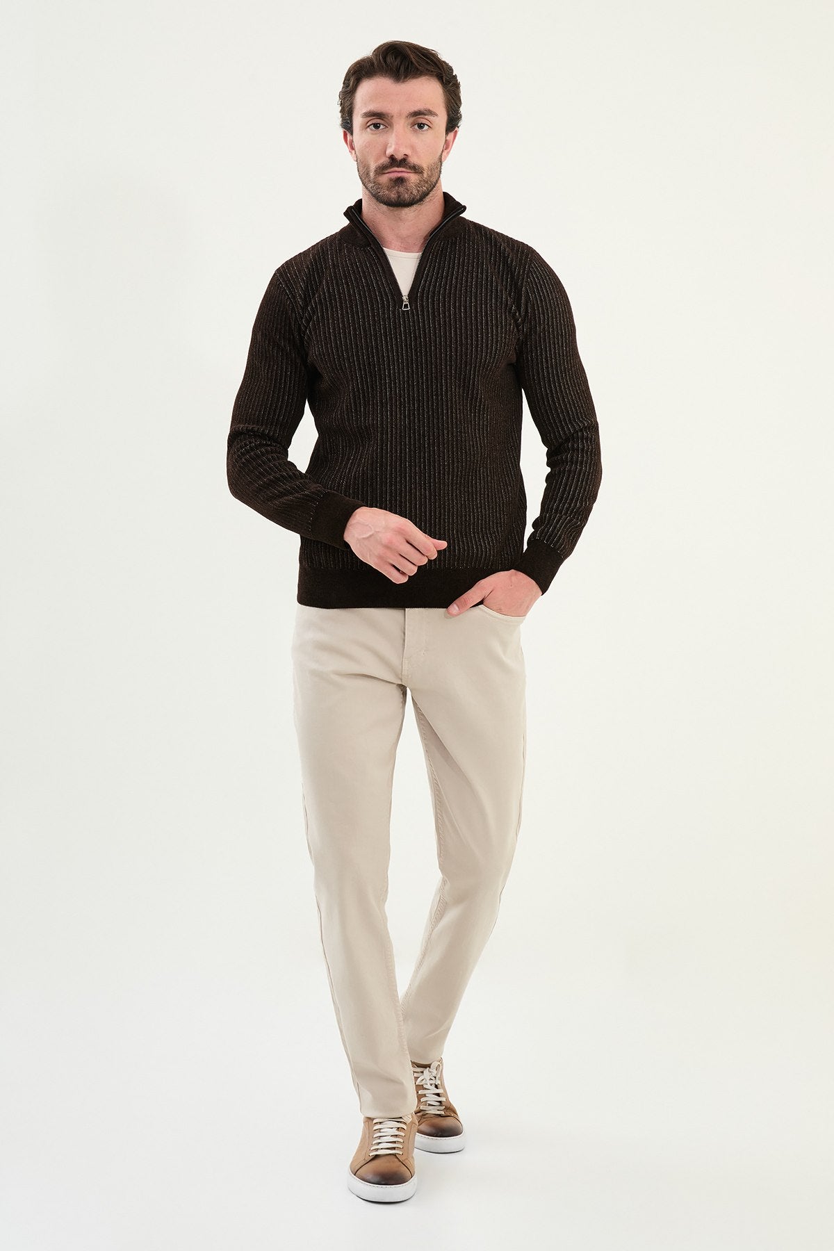 Man wearing a black patterned sweater and beige pants on a white background