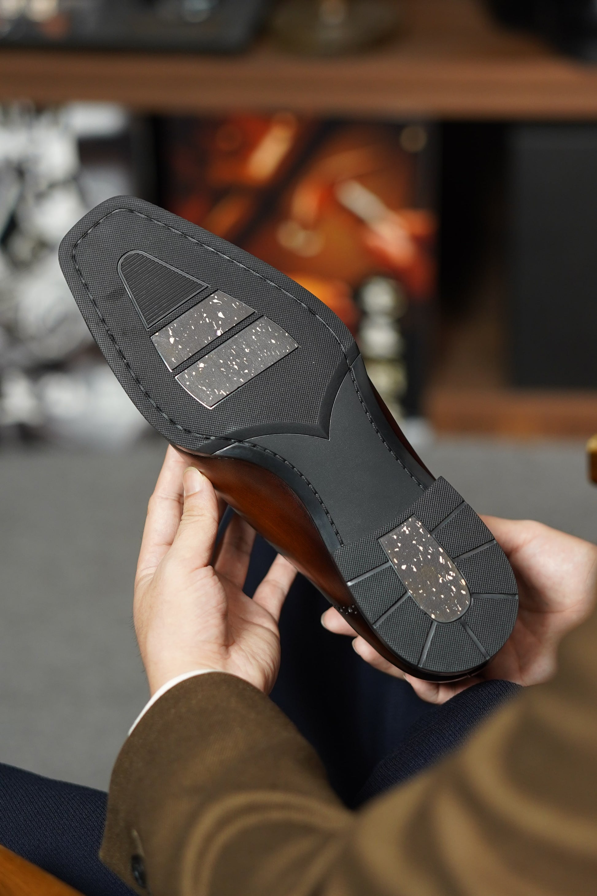 Close-up of a person holding a brown leather shoe with a focus on the sole.