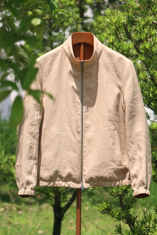A reversible linen bomber jacket in tan and clay colors, displayed on a stand outdoors with foliage in the background.