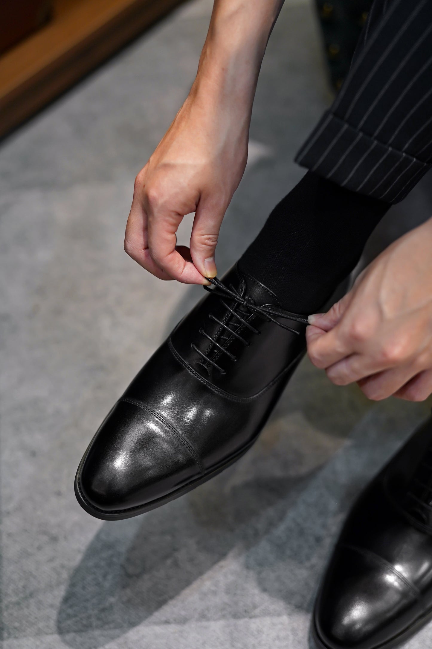 Close-up of men’s black leather cap-toe oxfords, worn with pinstriped trousers, showcasing classic formal design with lightweight and breathable construction for added comfort.