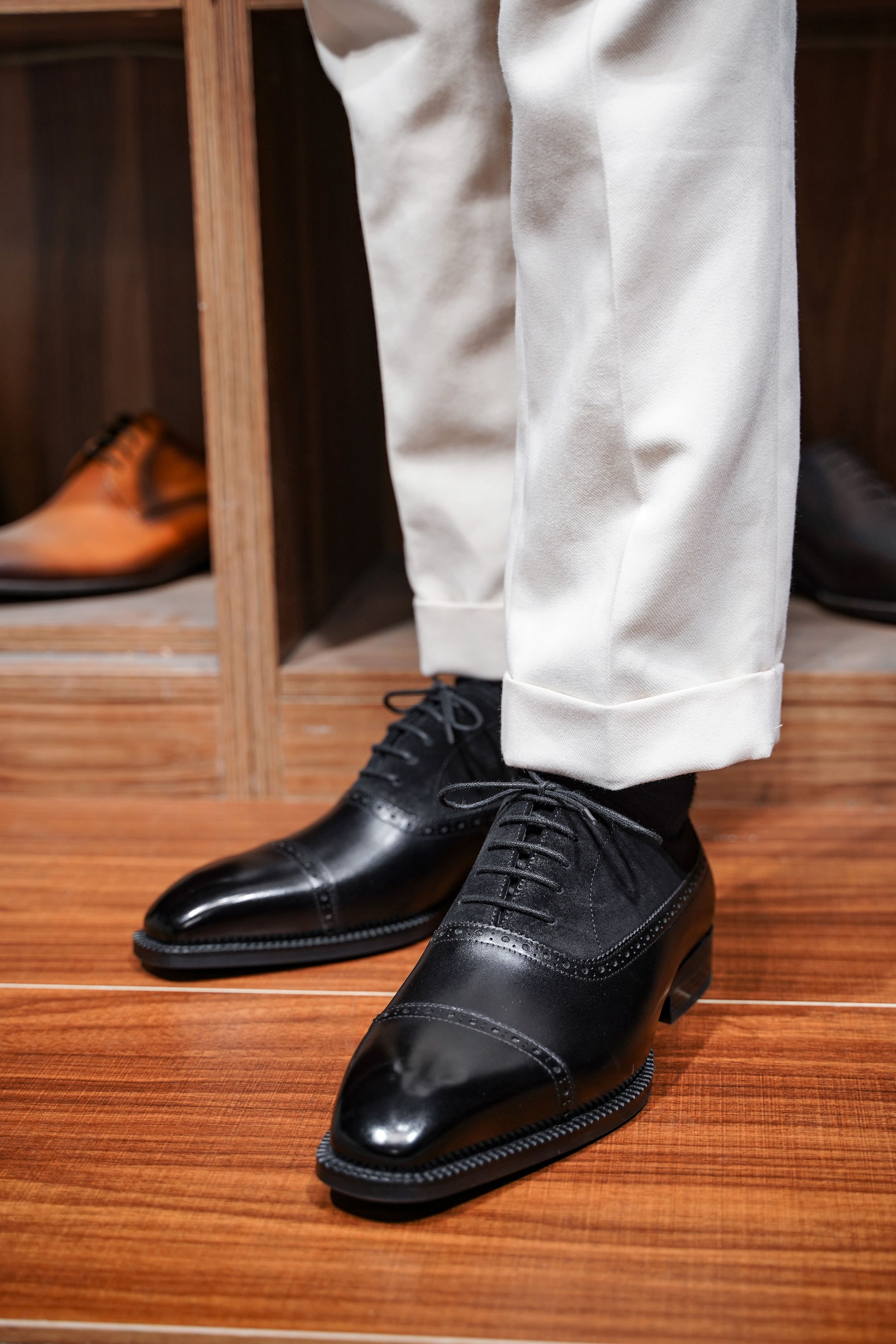 Close-up of men's black leather and suede oxfords with cap-toe detailing, showcasing a refined two-tone design perfect for formal attire.