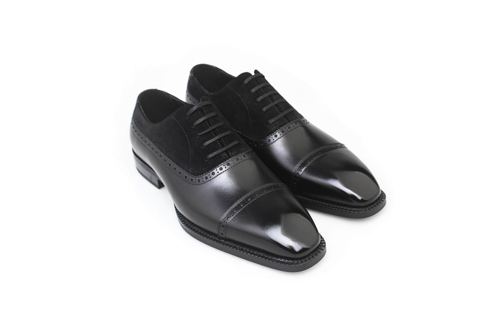 Close-up of men's black leather and suede oxfords with cap-toe detailing, showcasing a refined two-tone design perfect for formal attire.