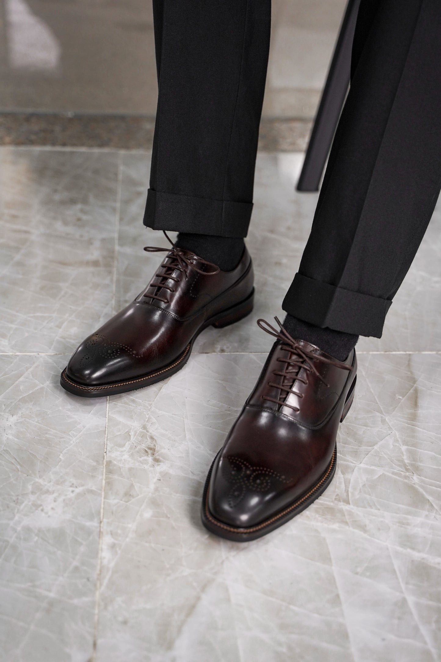 Close-up of men’s regal oxford shoes in rich brown leather with intricate brogue detailing, showcasing luxurious craftsmanship and a timeless design for formal wear.