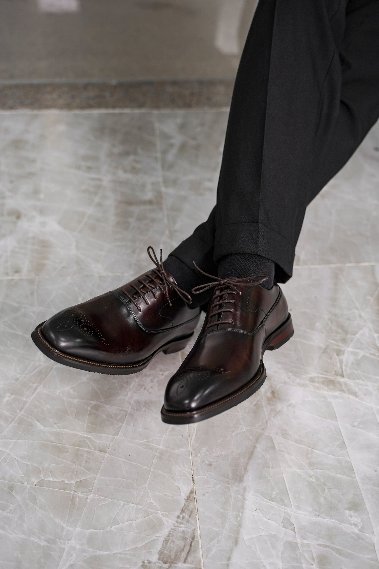 Close-up of men’s regal oxford shoes in rich brown leather with intricate brogue detailing, showcasing luxurious craftsmanship and a timeless design for formal wear.