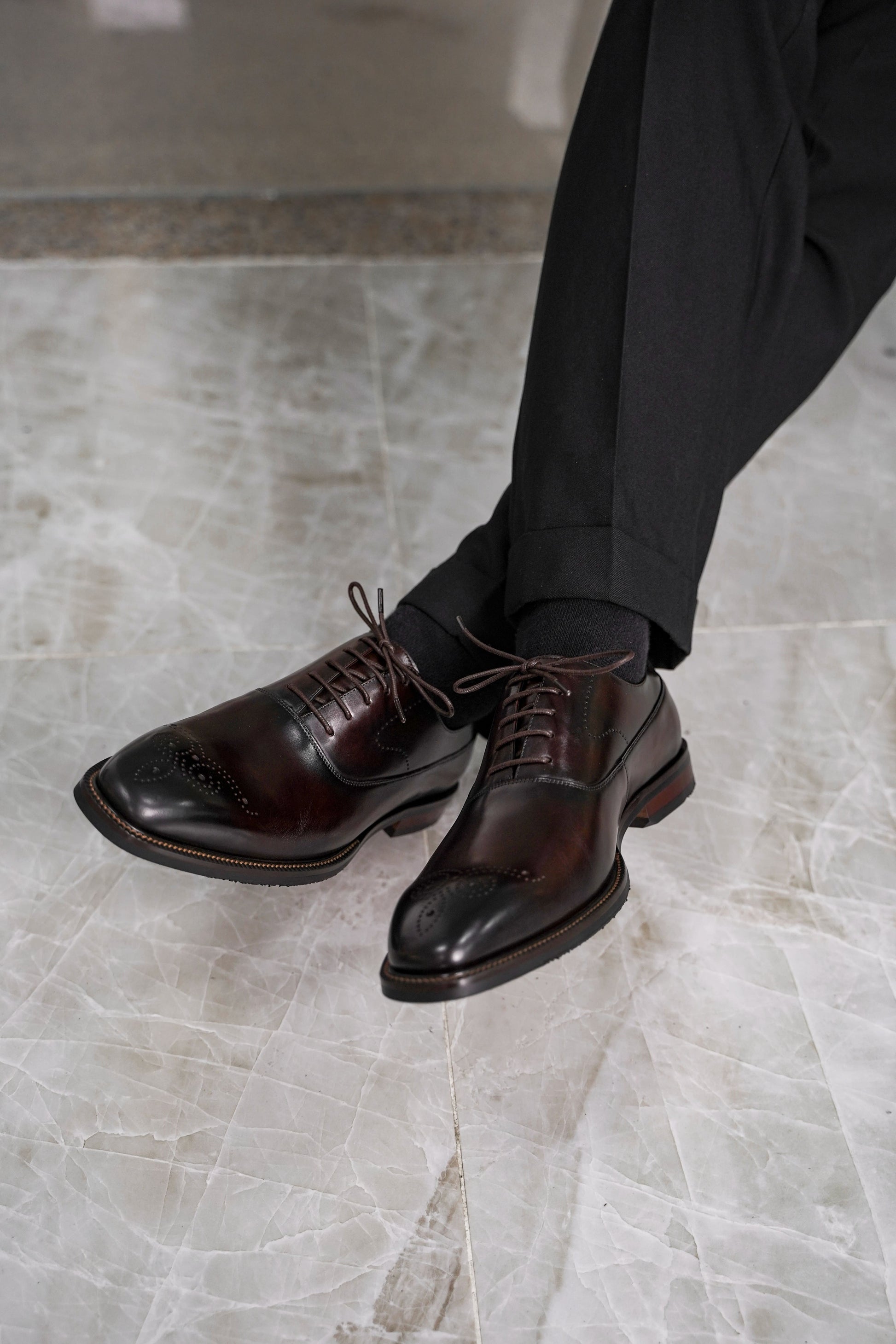 Close-up of men’s regal oxford shoes in rich brown leather with intricate brogue detailing, showcasing luxurious craftsmanship and a timeless design for formal wear.