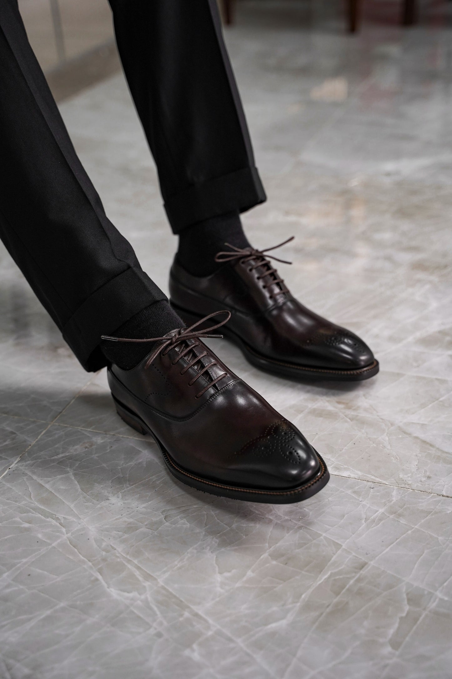 Close-up of men’s regal oxford shoes in rich brown leather with intricate brogue detailing, showcasing luxurious craftsmanship and a timeless design for formal wear.
