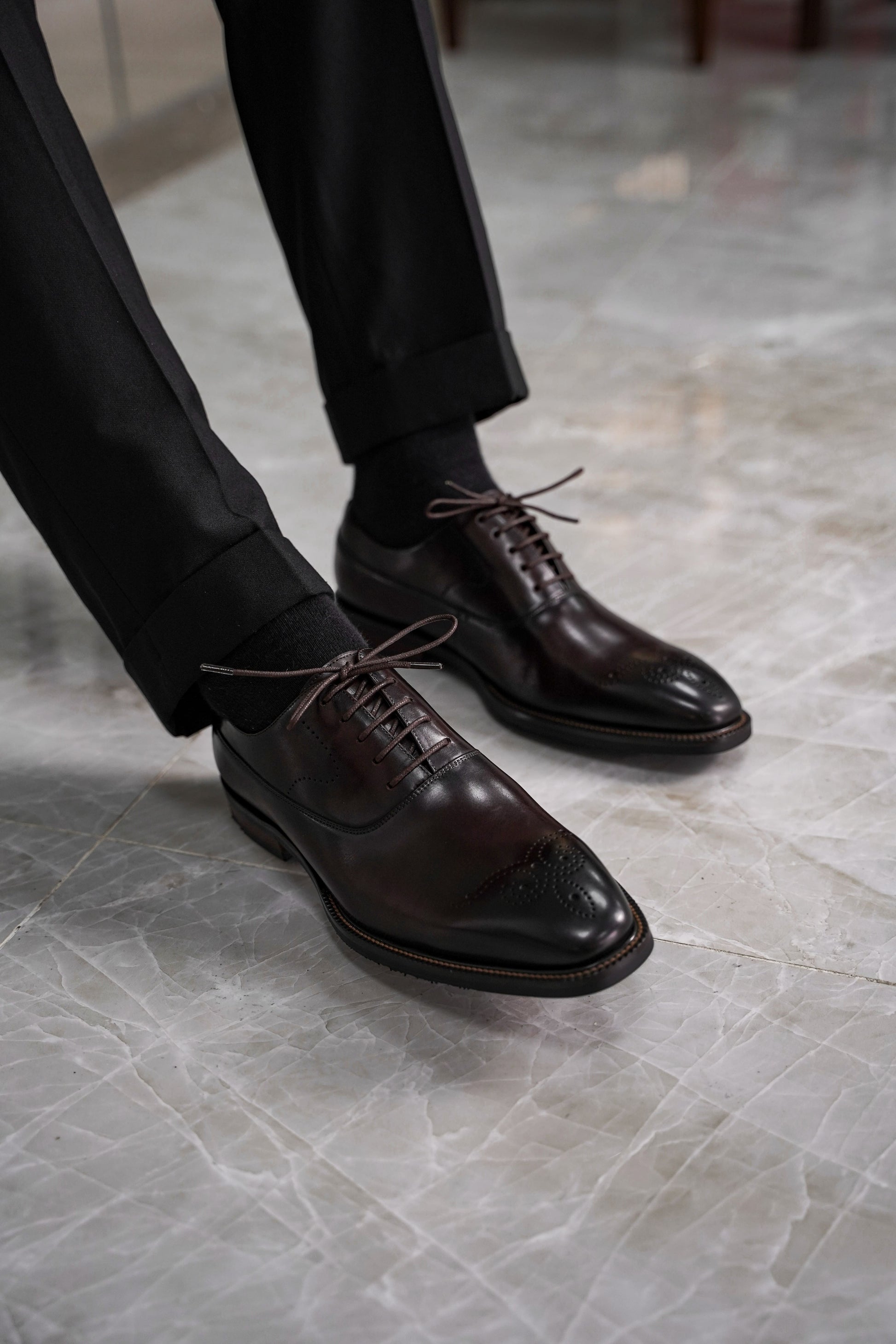 Close-up of men’s regal oxford shoes in rich brown leather with intricate brogue detailing, showcasing luxurious craftsmanship and a timeless design for formal wear.