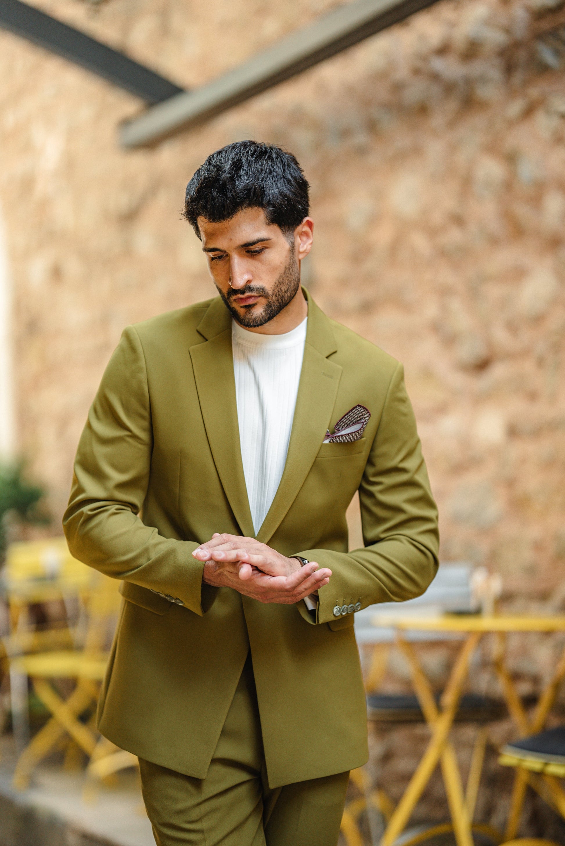 Man wearing a green suit with a white shirt and patterned pocket square, standing in an outdoor setting.
