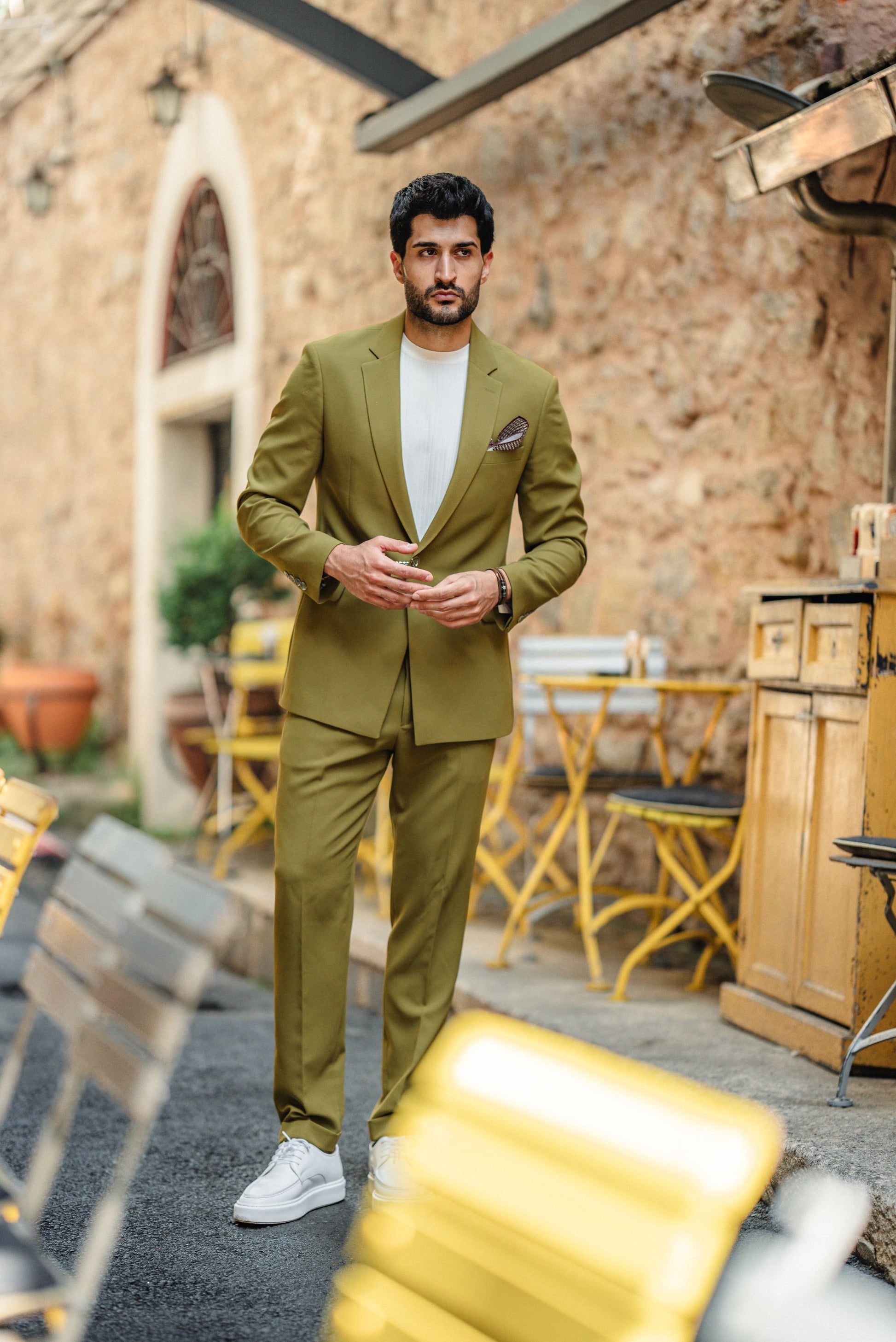 Man in a green suit standing outdoors with a rustic background