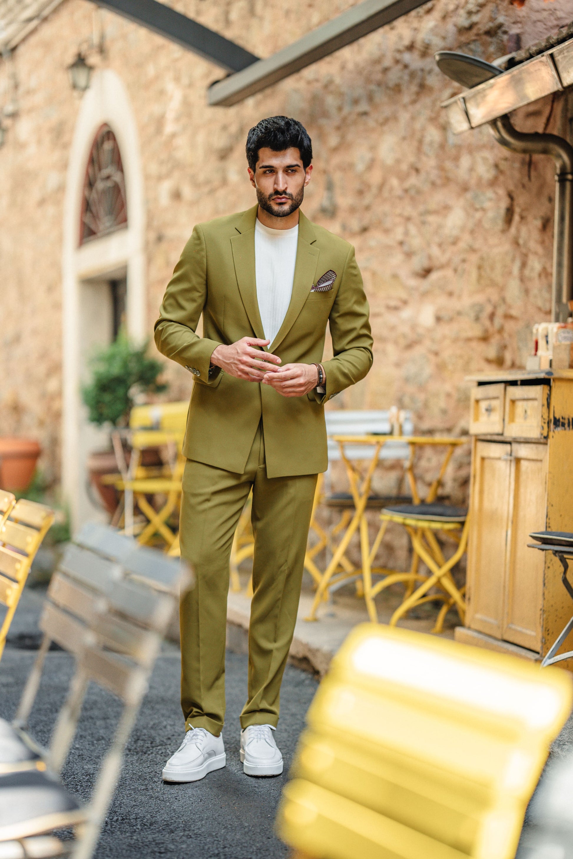 Man in a green suit standing outdoors with a rustic background