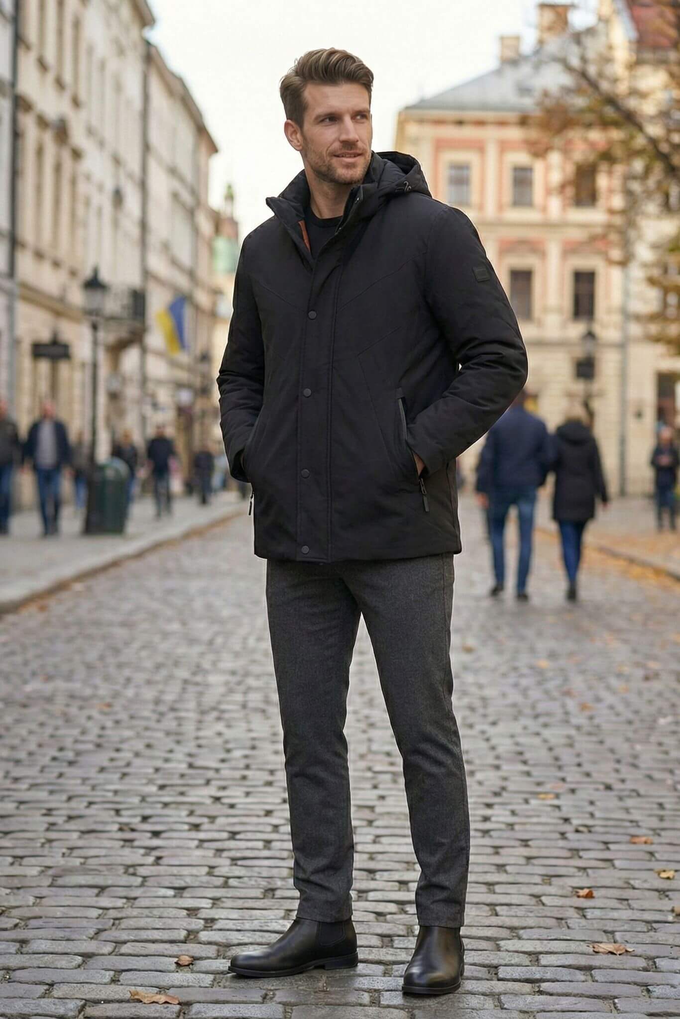 Man wearing a black coat standing on a cobblestone street with buildings in the background
