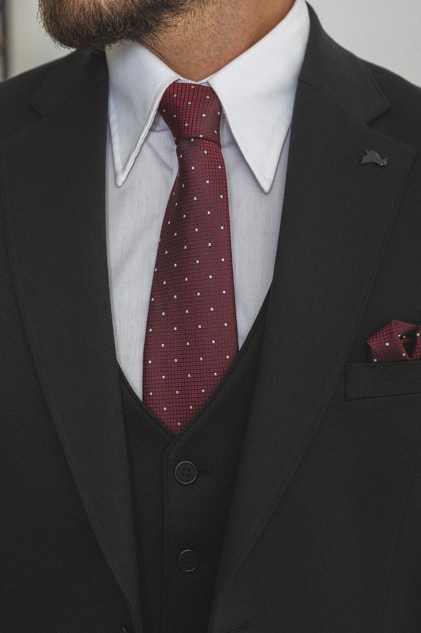 Man in a black 3-piece suit with a burgundy tie and pocket square.