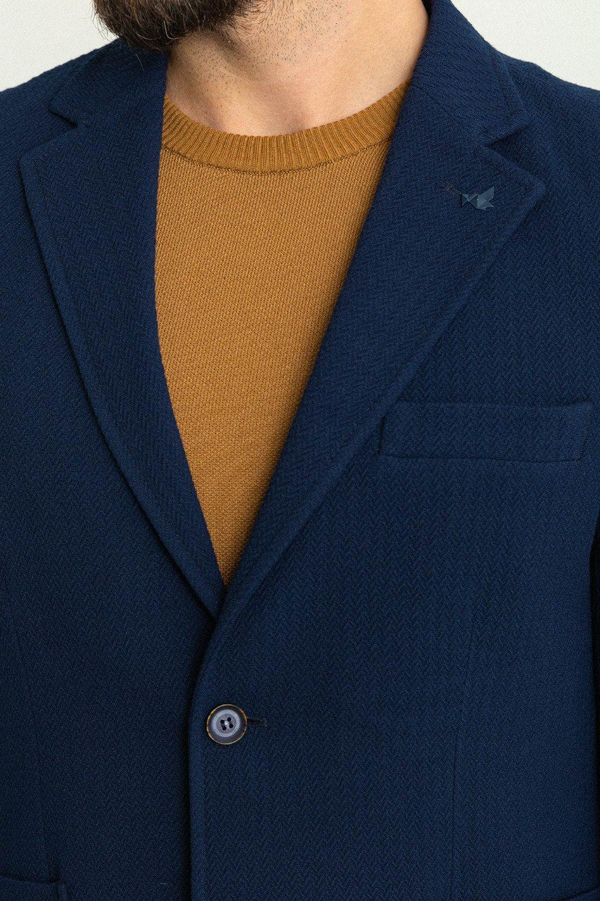 Man wearing a navy blue blazer paired with a mustard sweater and brown trousers.