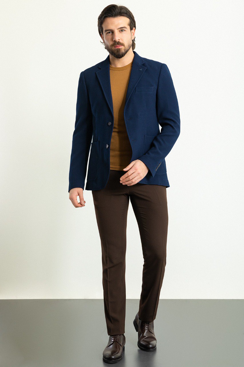 Man wearing a navy blue blazer paired with a mustard sweater and brown trousers.
