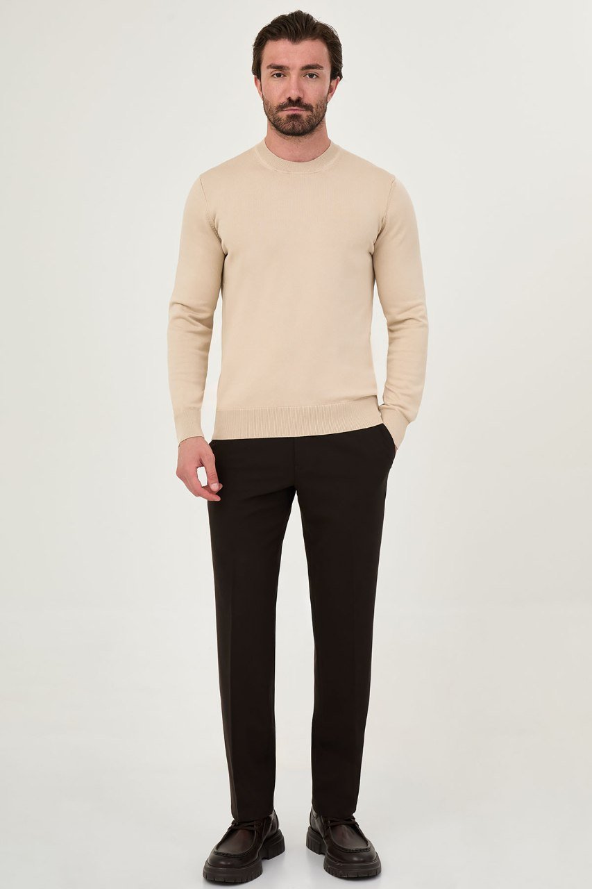 Man wearing a beige crew neck sweater with black trousers