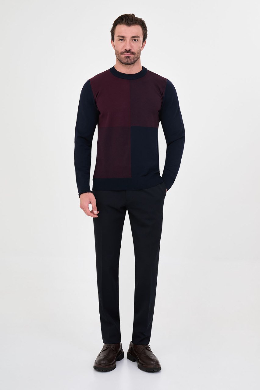 Man wearing a navy blue and burgundy colour-block sweater with black trousers