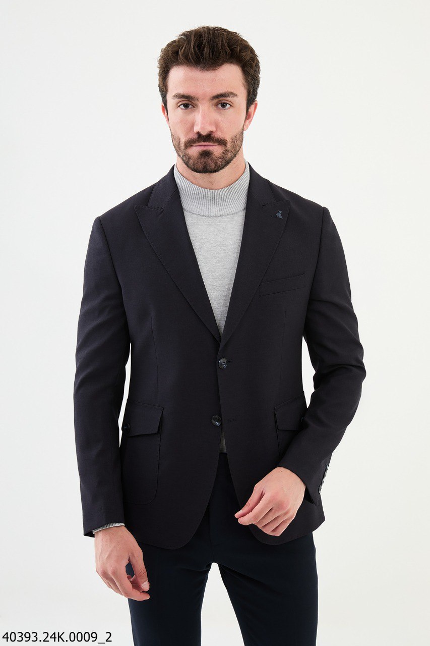 A man wearing a black formal blazer with a slim fit, paired with a grey sweater and blue jeans.