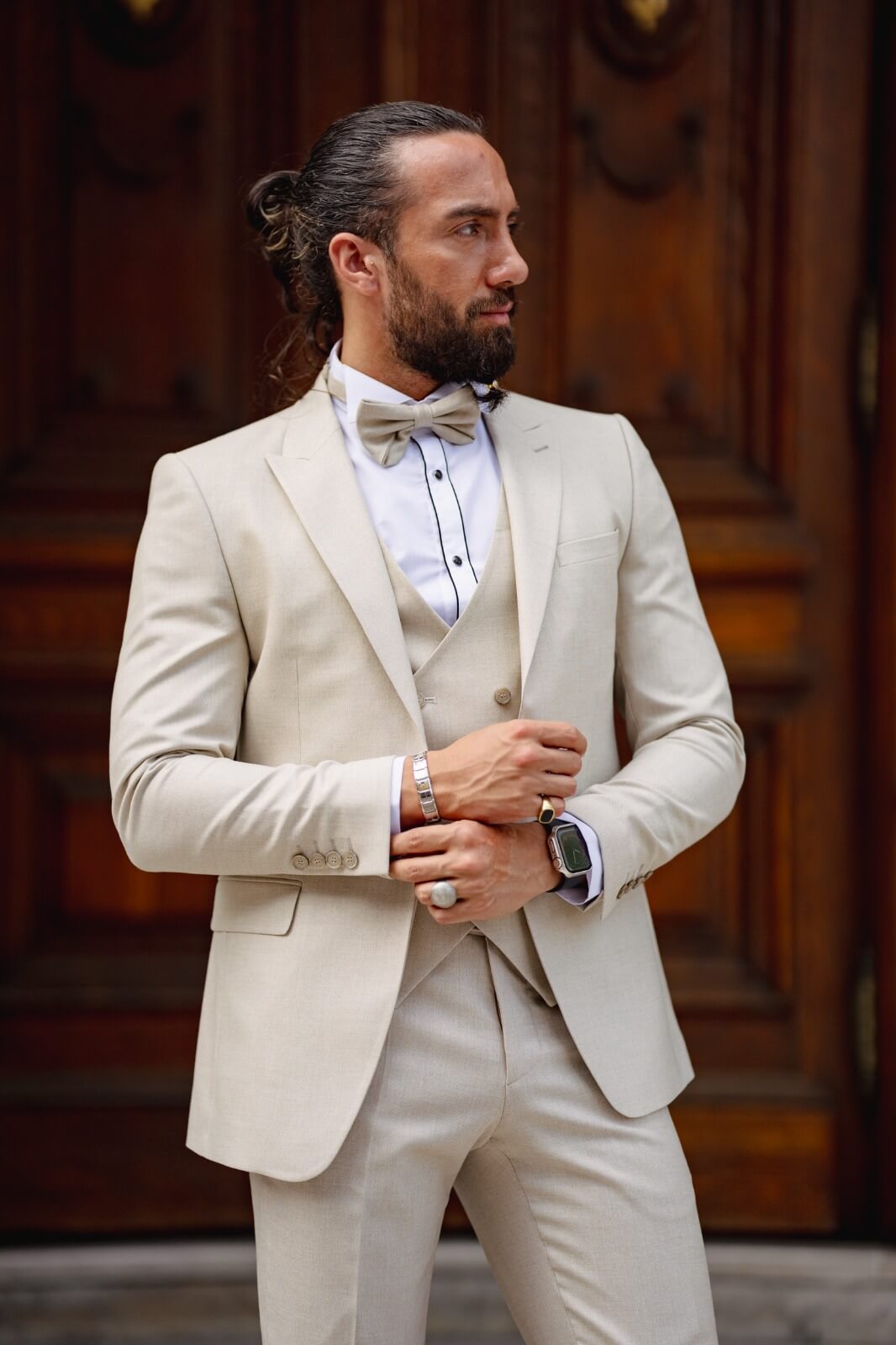 A bearded man posing in a Birch Beige Tuxedo Suit in front of a door