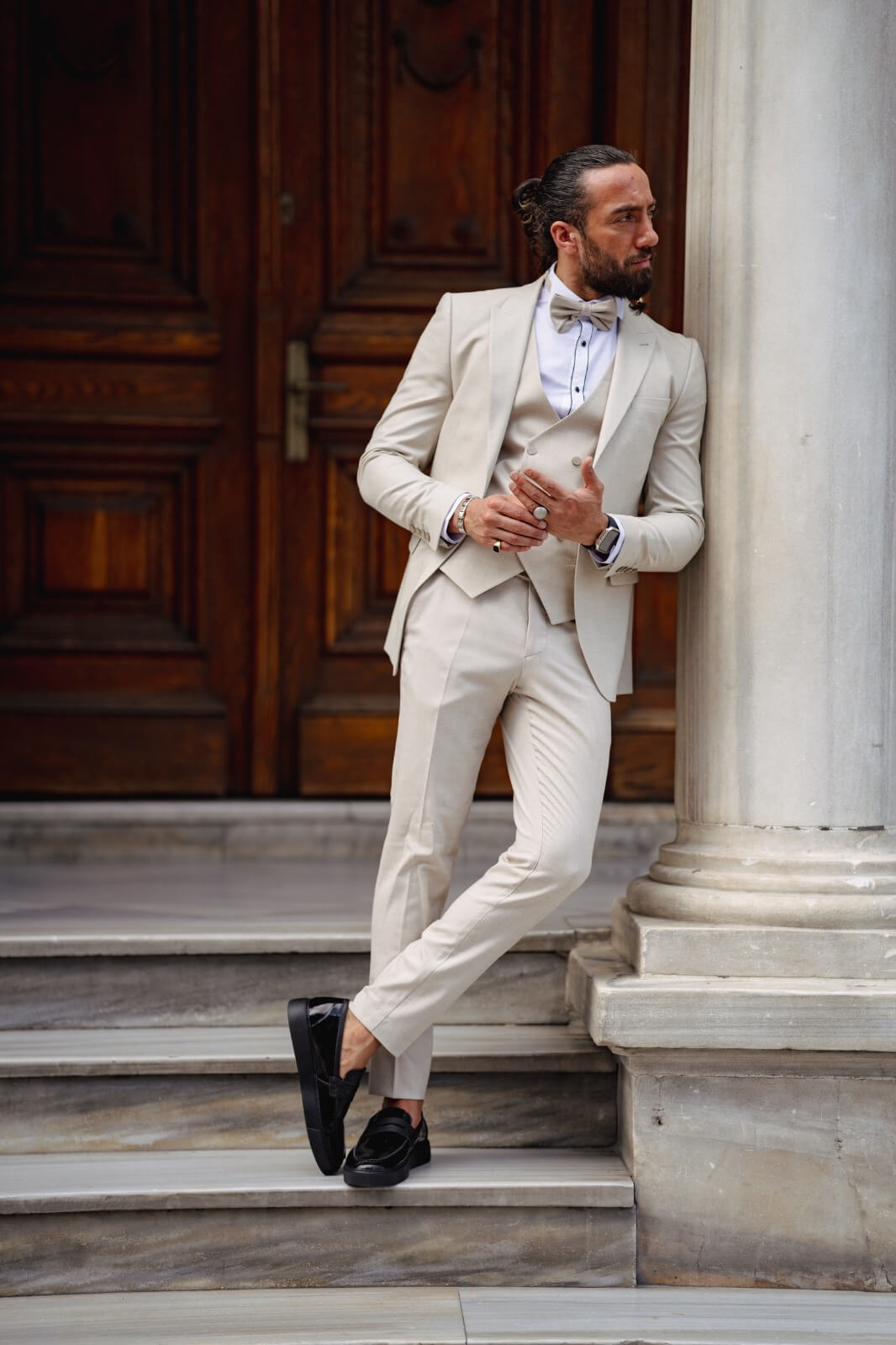 A man in a Birch Beige Tuxedo Suit leaning against a pillar