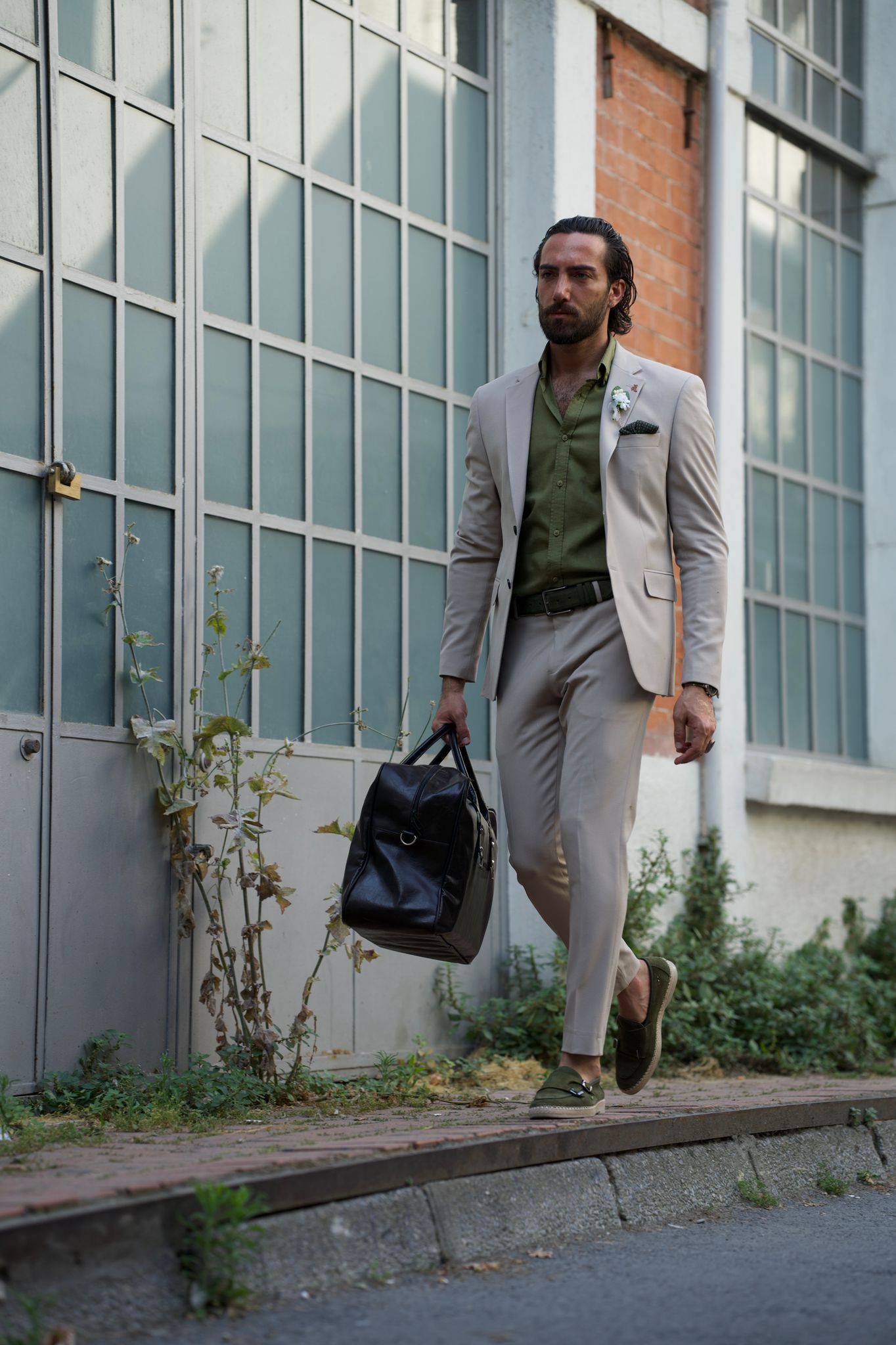 Model wearing a beige suit with black bag, posing confidently.