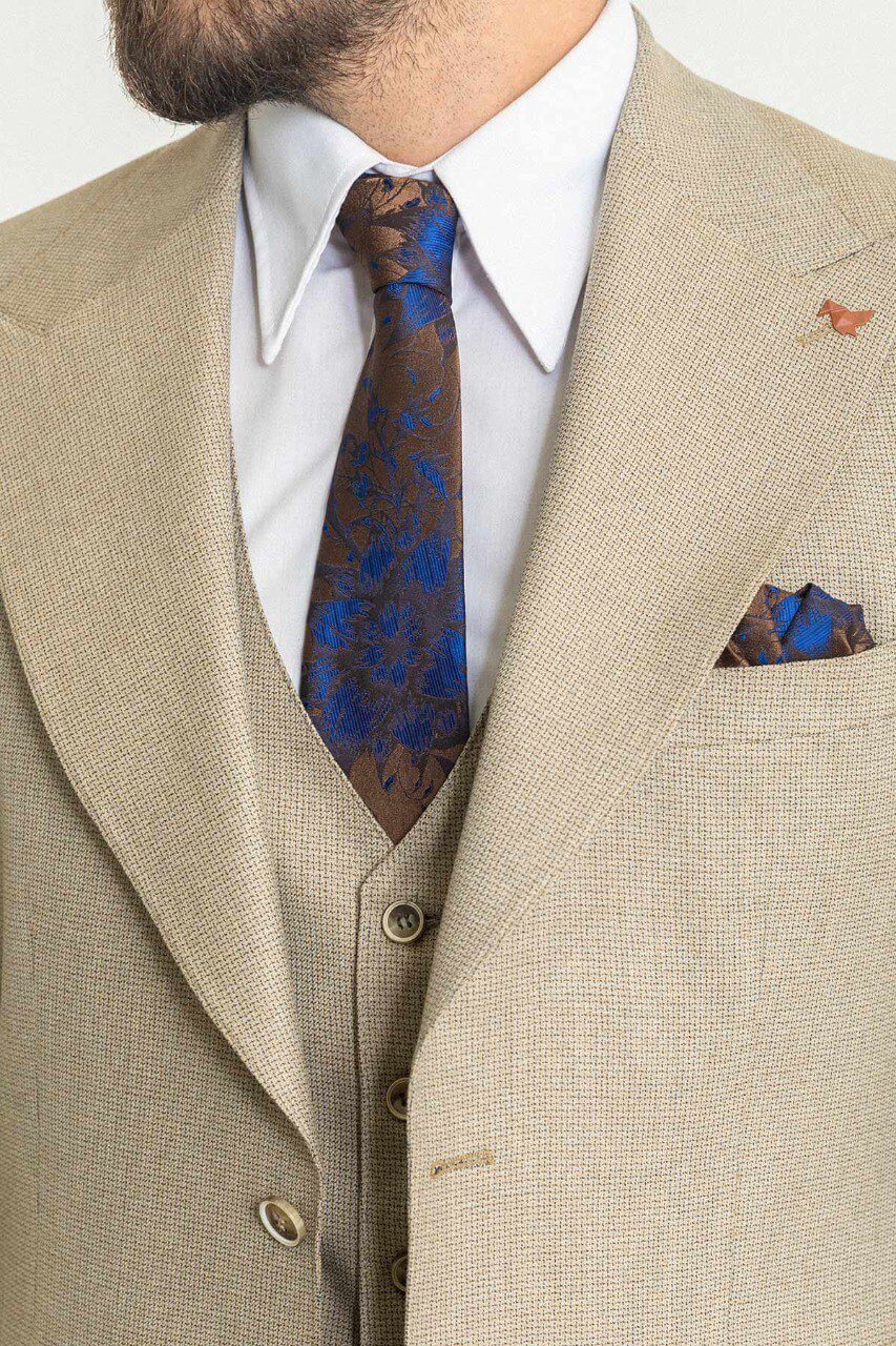 Man in a plaid beige 3-piece suit with a blue tie and pocket square.