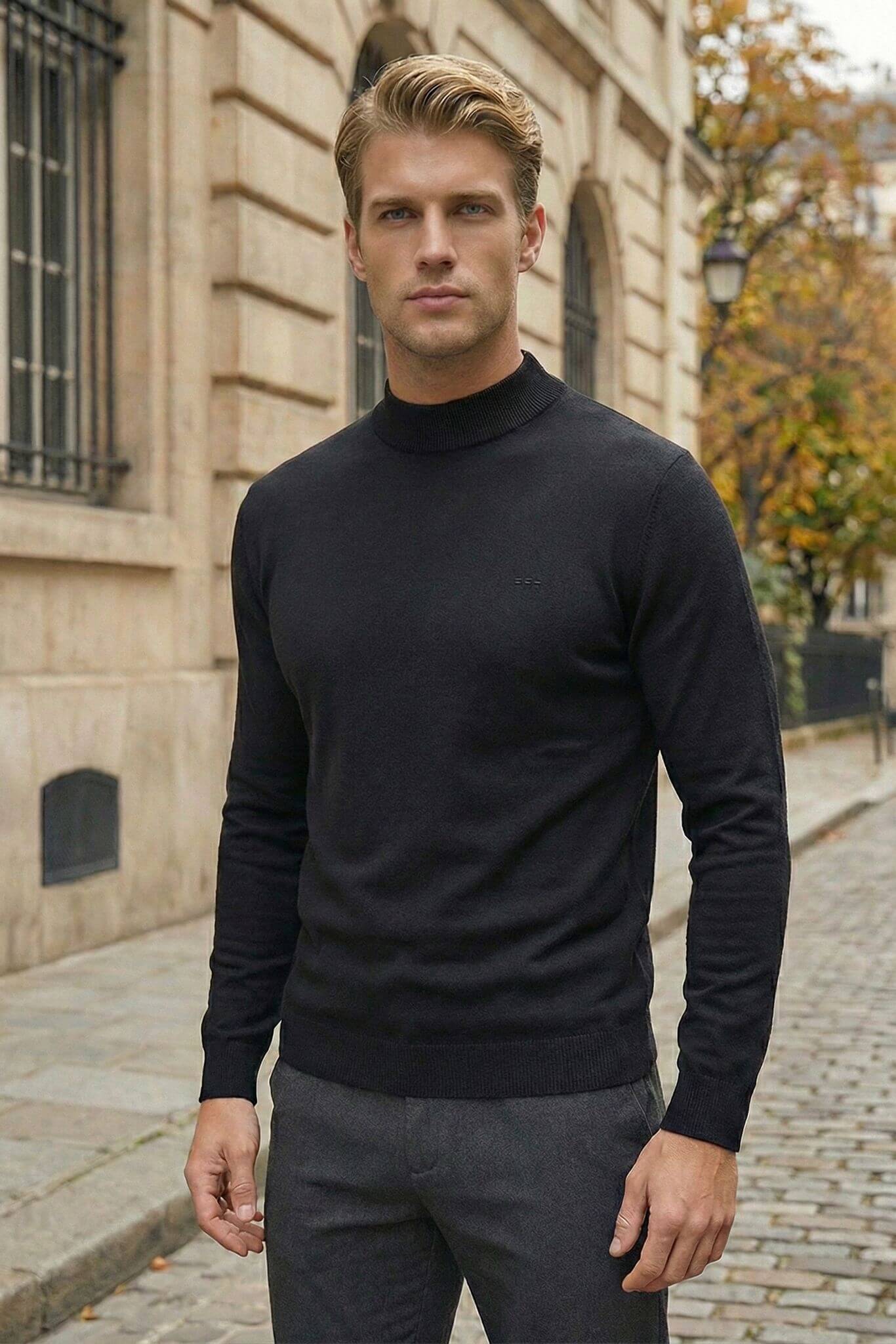 Man wearing a black turtleneck sweater and gray pants standing on a street.