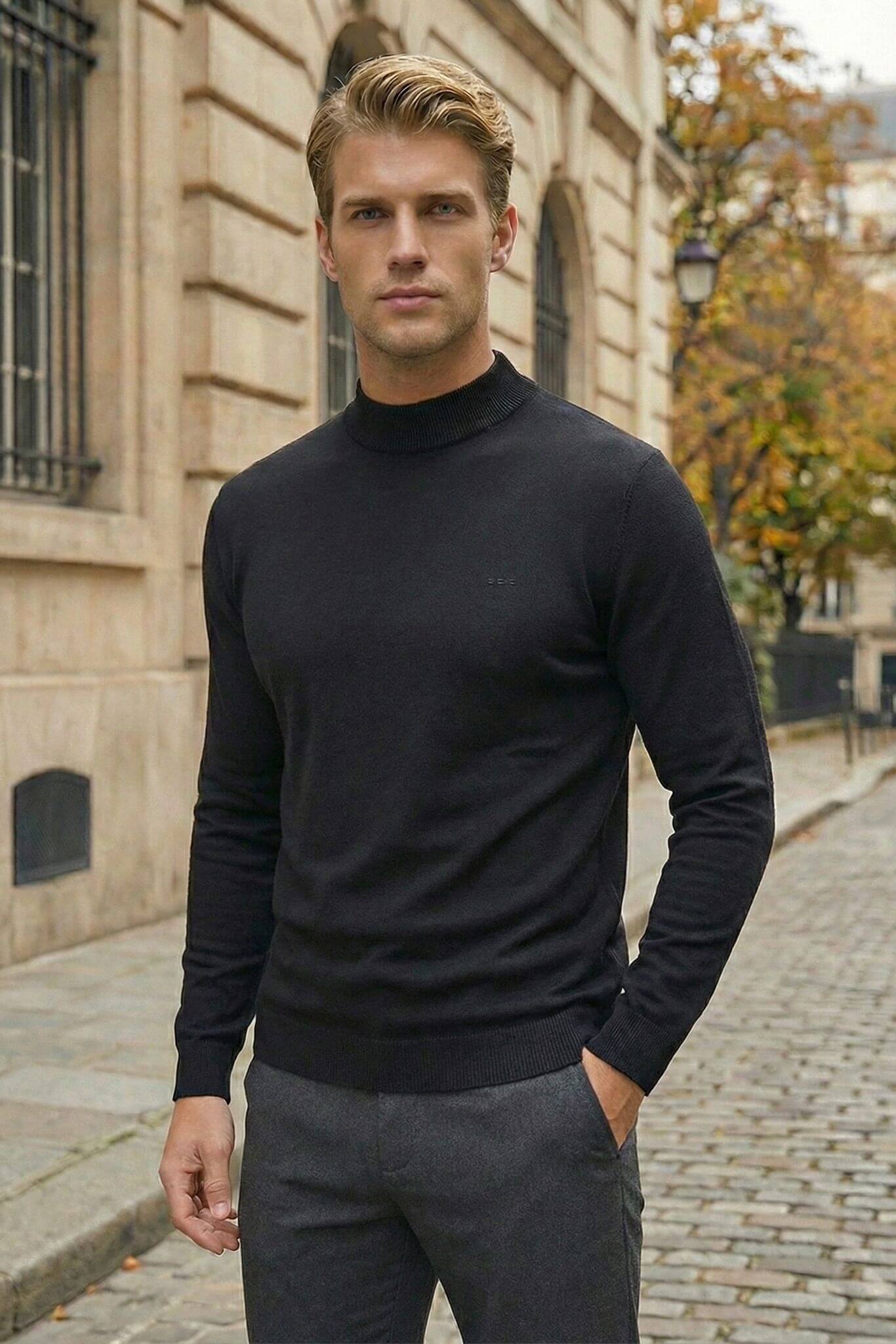 Man wearing a black turtleneck sweater and gray pants standing on a street.
