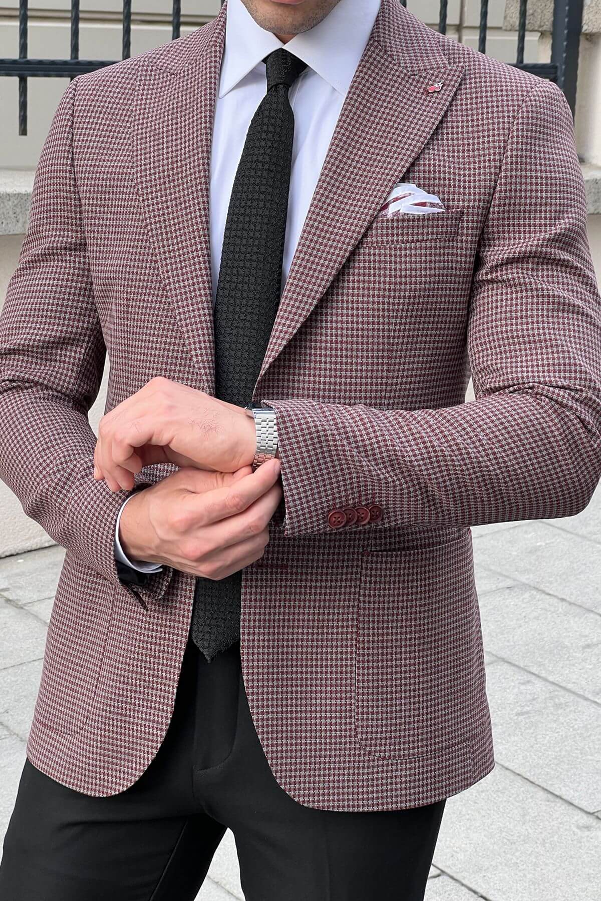 Man wearing a checkered suit jacket with a white shirt and black tie outdoors.