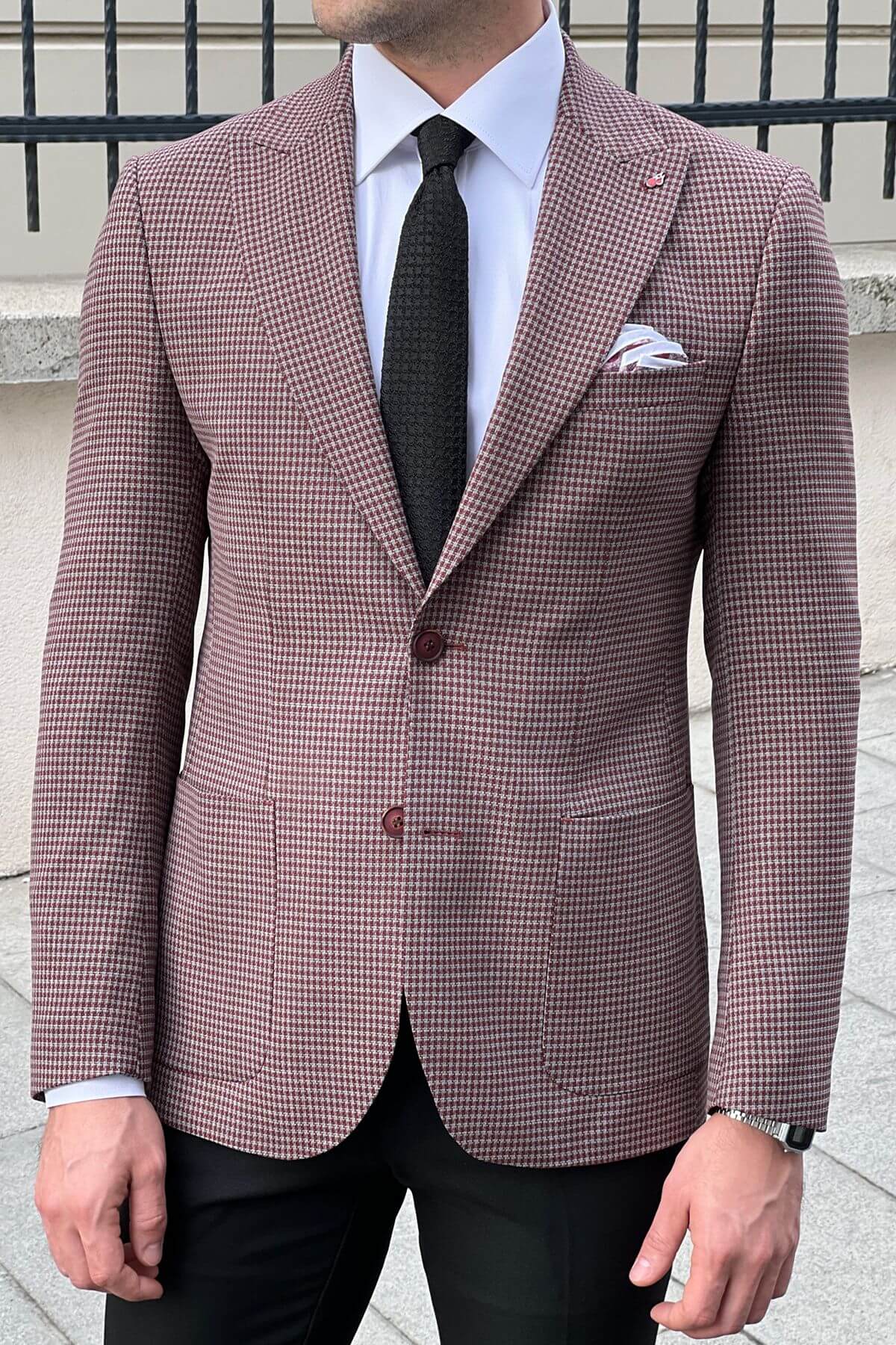 Man wearing a brown checkered blazer with a white shirt and black tie.