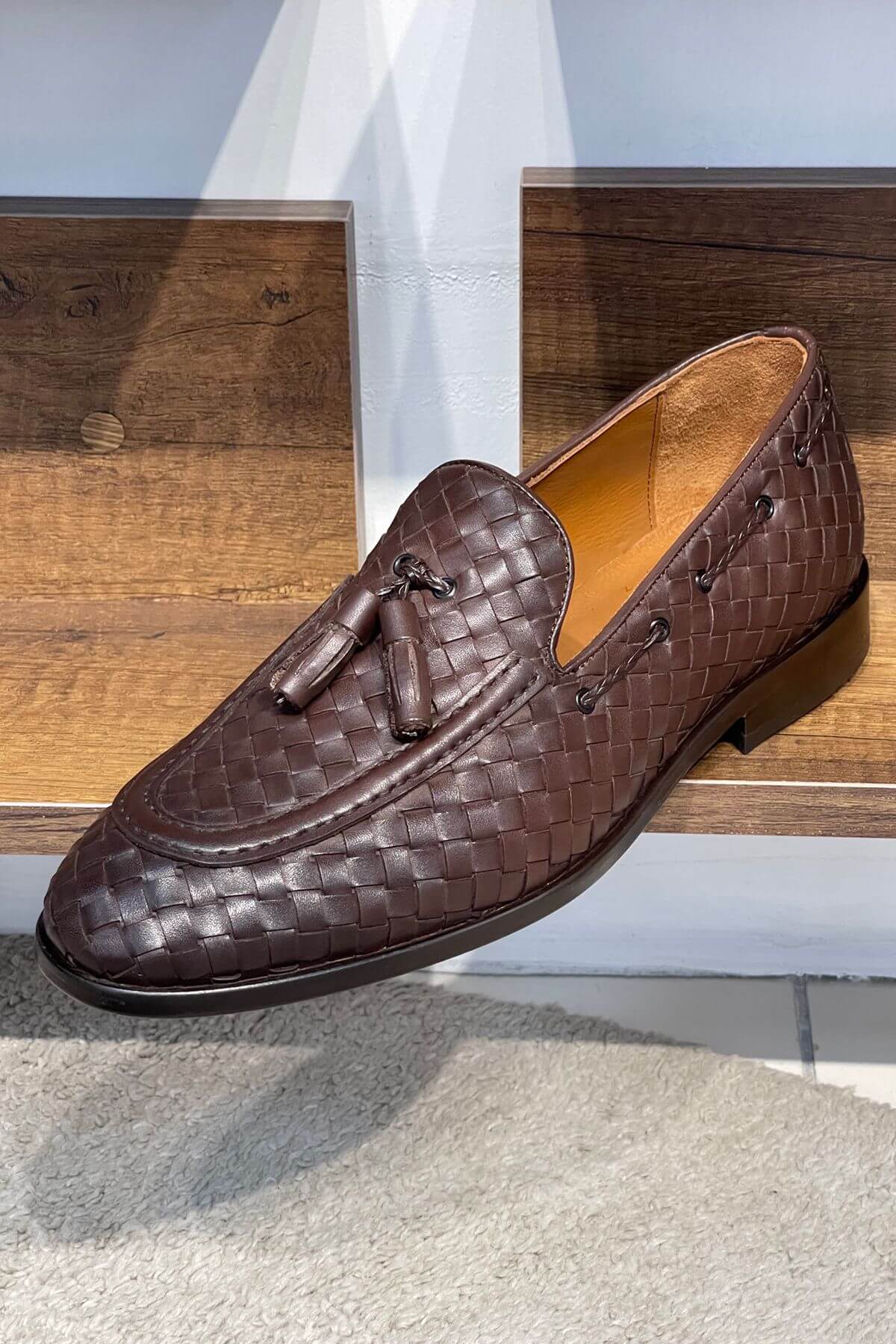 Brown woven loafer with tassel on a wooden surface