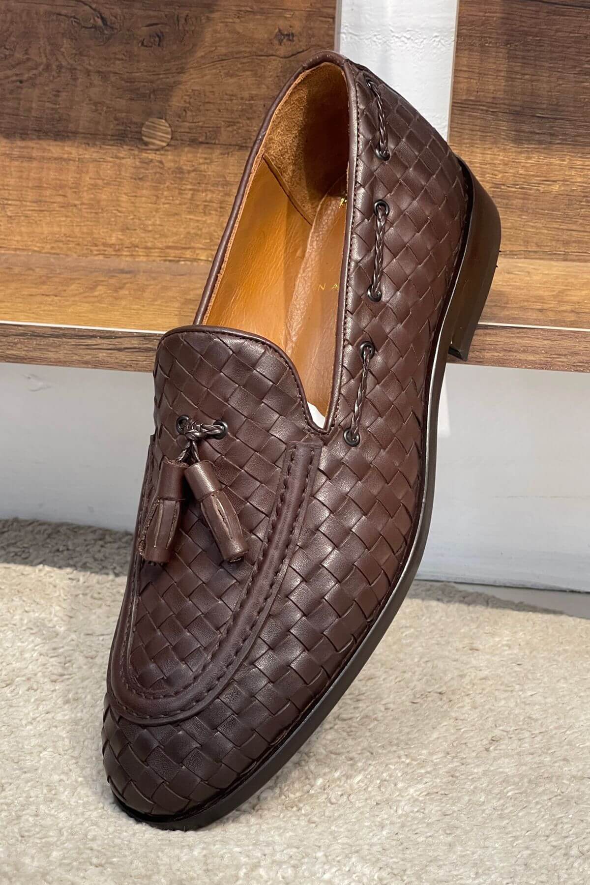 Brown woven loafer with tassel on a wooden surface