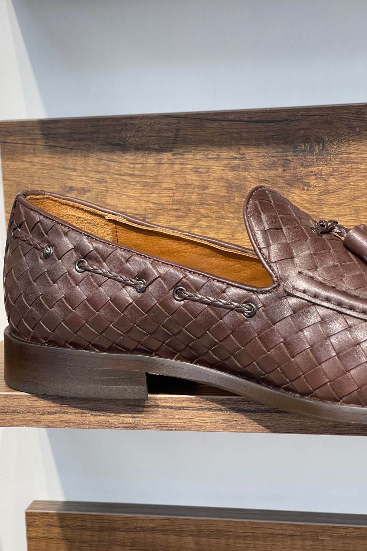 Brown woven loafer on a wooden shelf