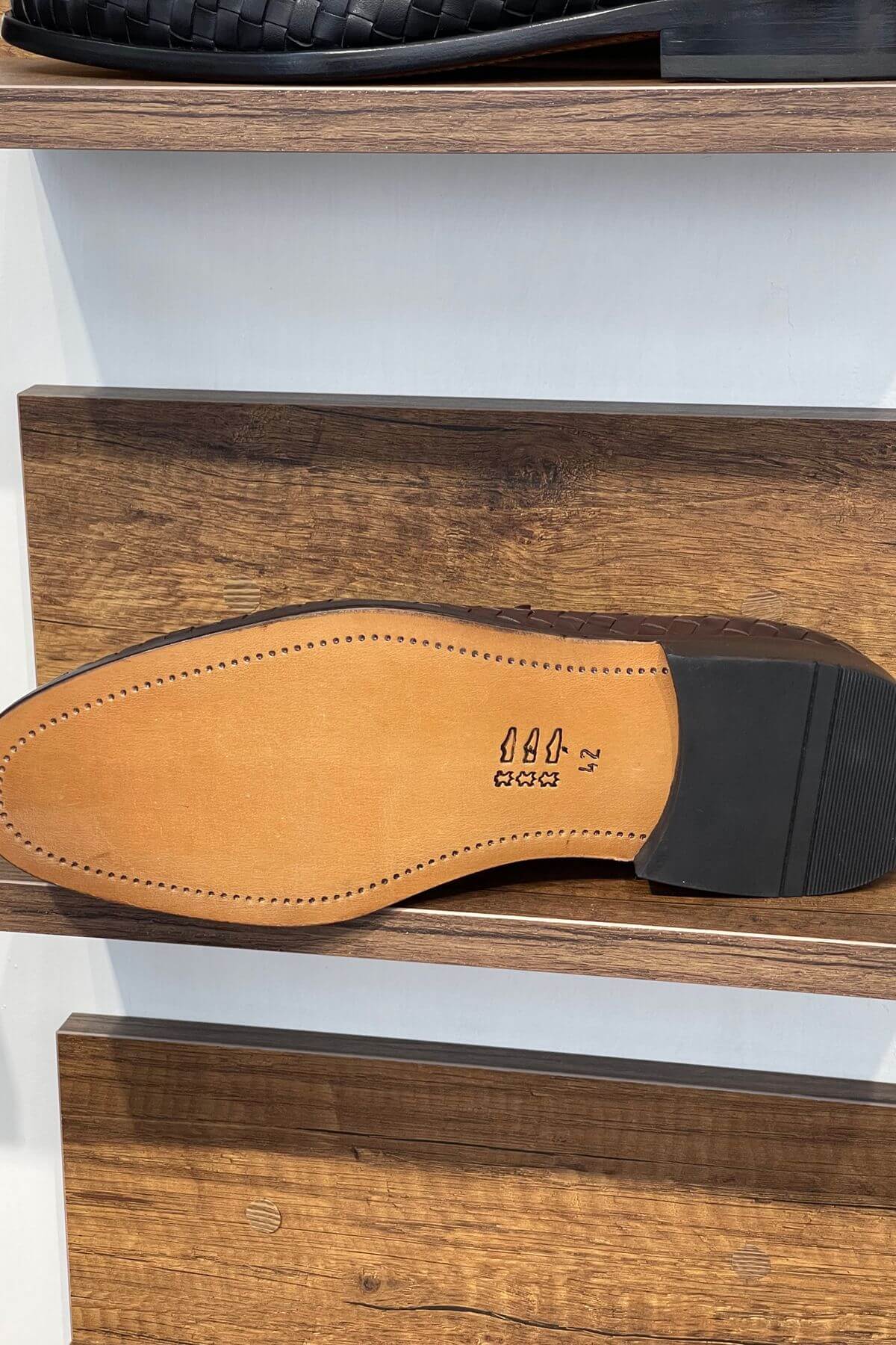 Close-up of a shoe sole with a brand logo on a wooden shelf.