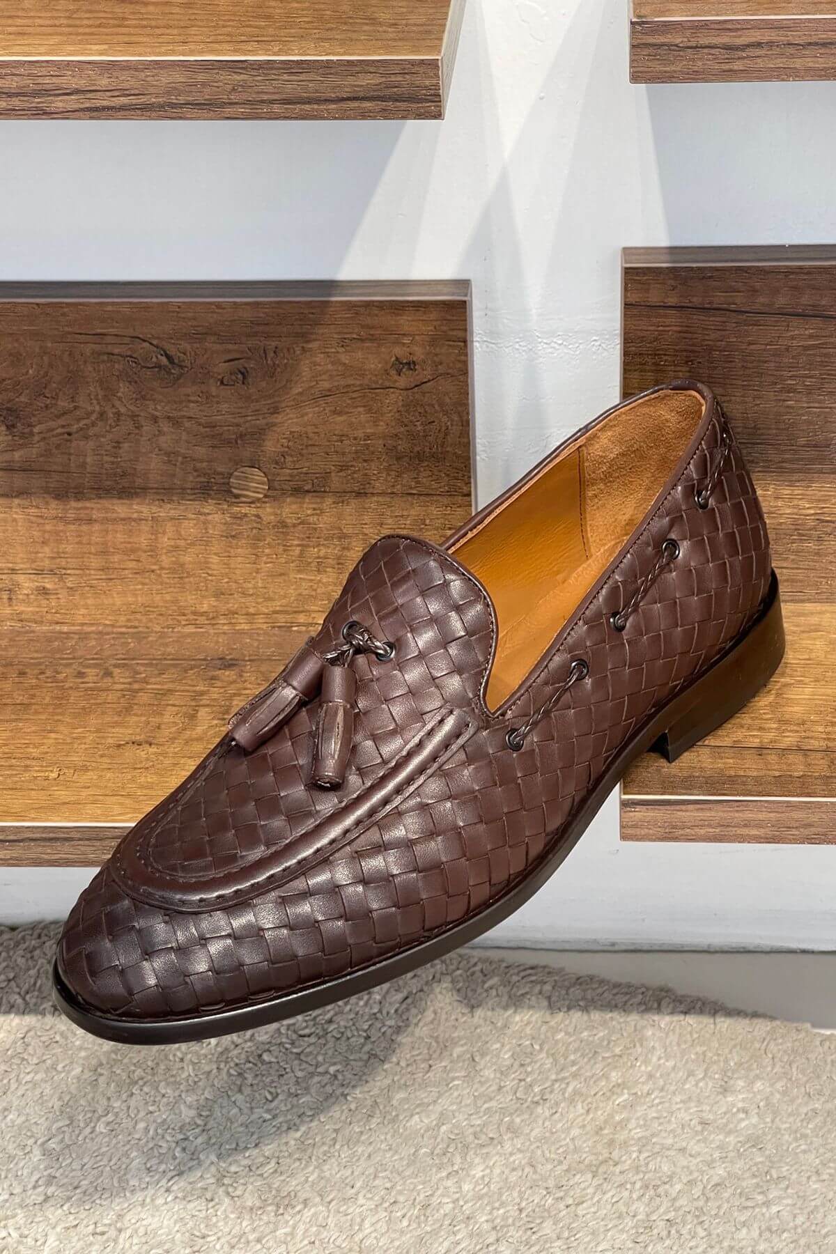 Brown woven loafer with tassels on a wooden floor
