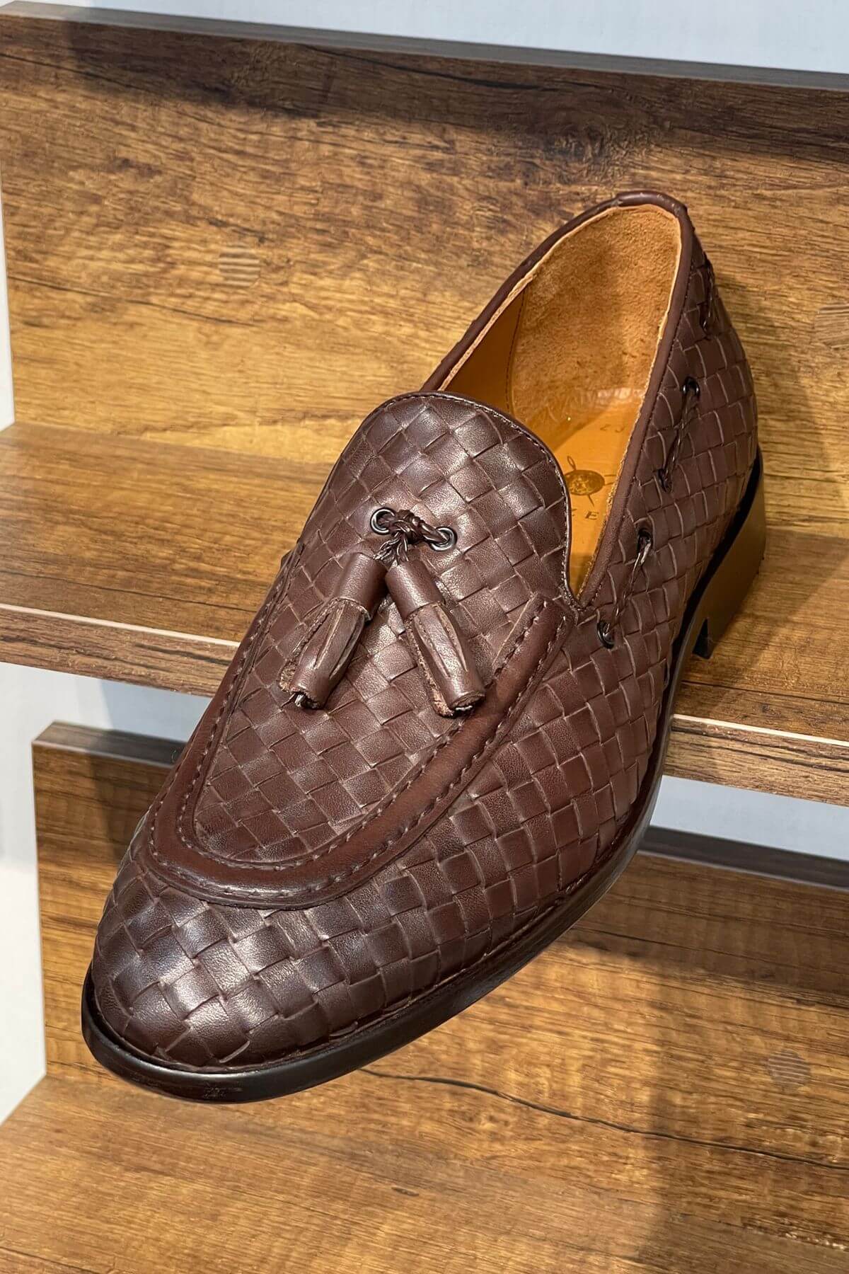Brown woven loafer with tassel on a wooden surface