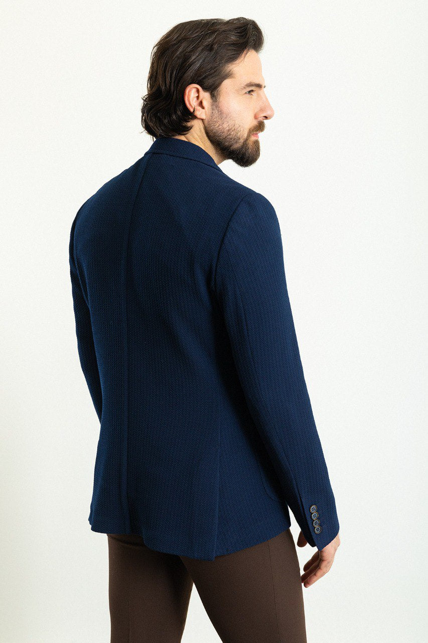 Man wearing a navy blue blazer paired with a mustard sweater and brown trousers.