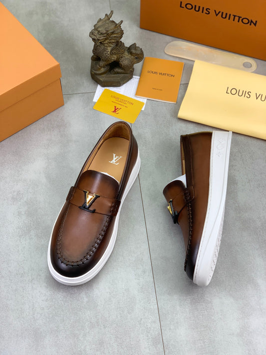 A pair of Louis Vuitton brown leather slip-on loafers with white platform soles, displayed on a gray floor alongside their signature orange and beige Louis Vuitton packaging boxes, dust bag, and cards.