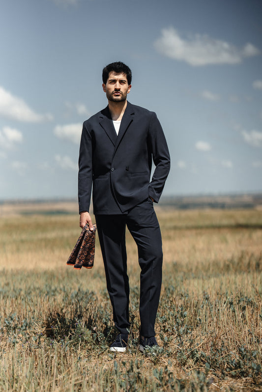 Man in a dark suit standing in a field with a clear sky.