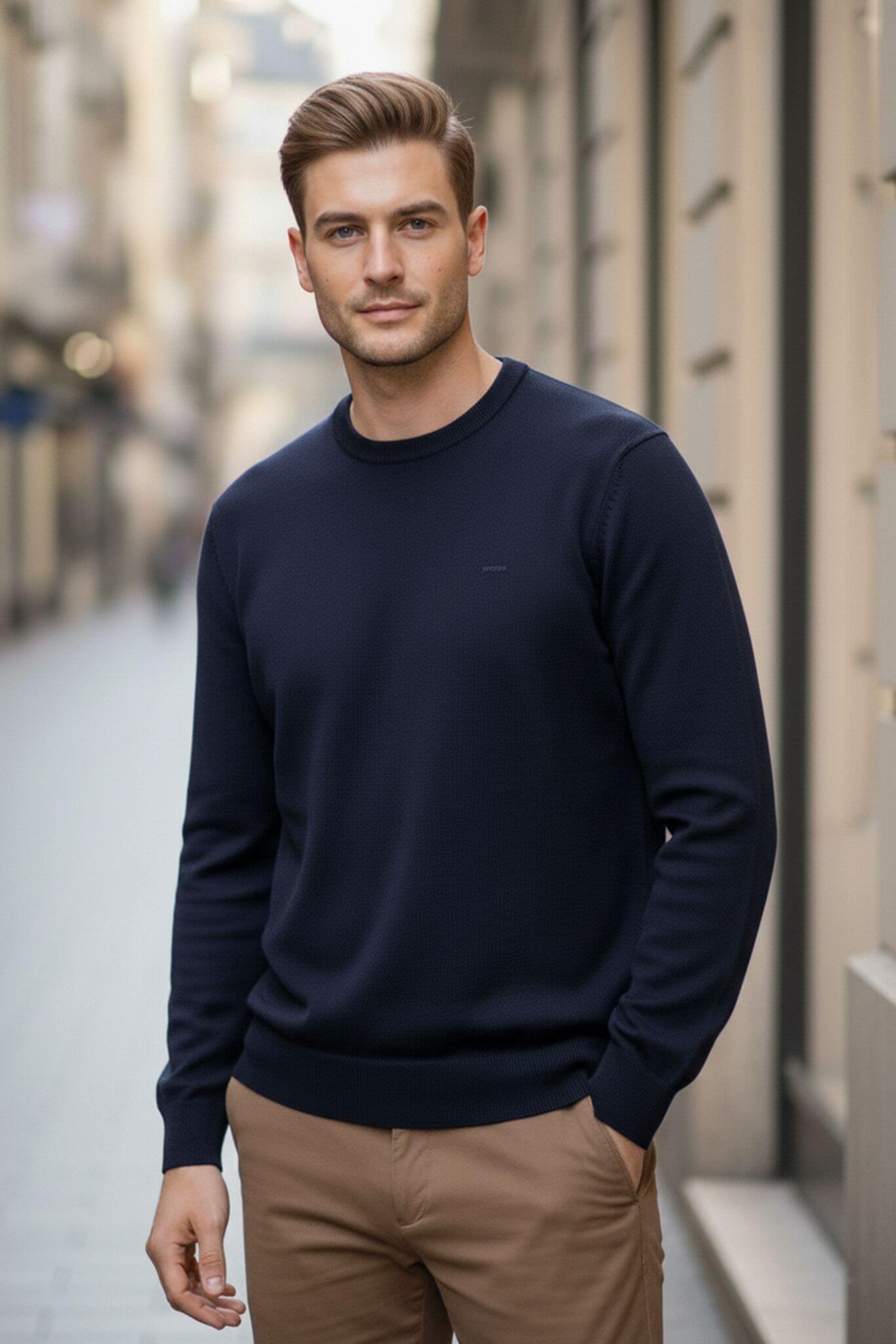 Man wearing a navy sweater and beige pants standing on a city street.