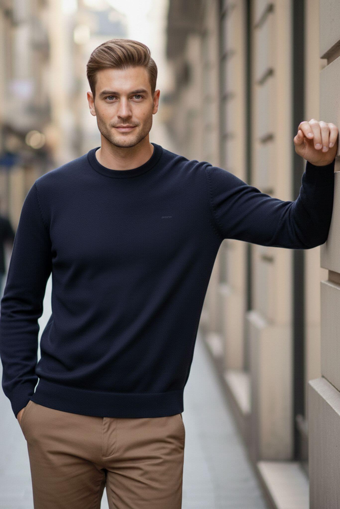 Man wearing a navy sweater and beige pants standing against an urban background